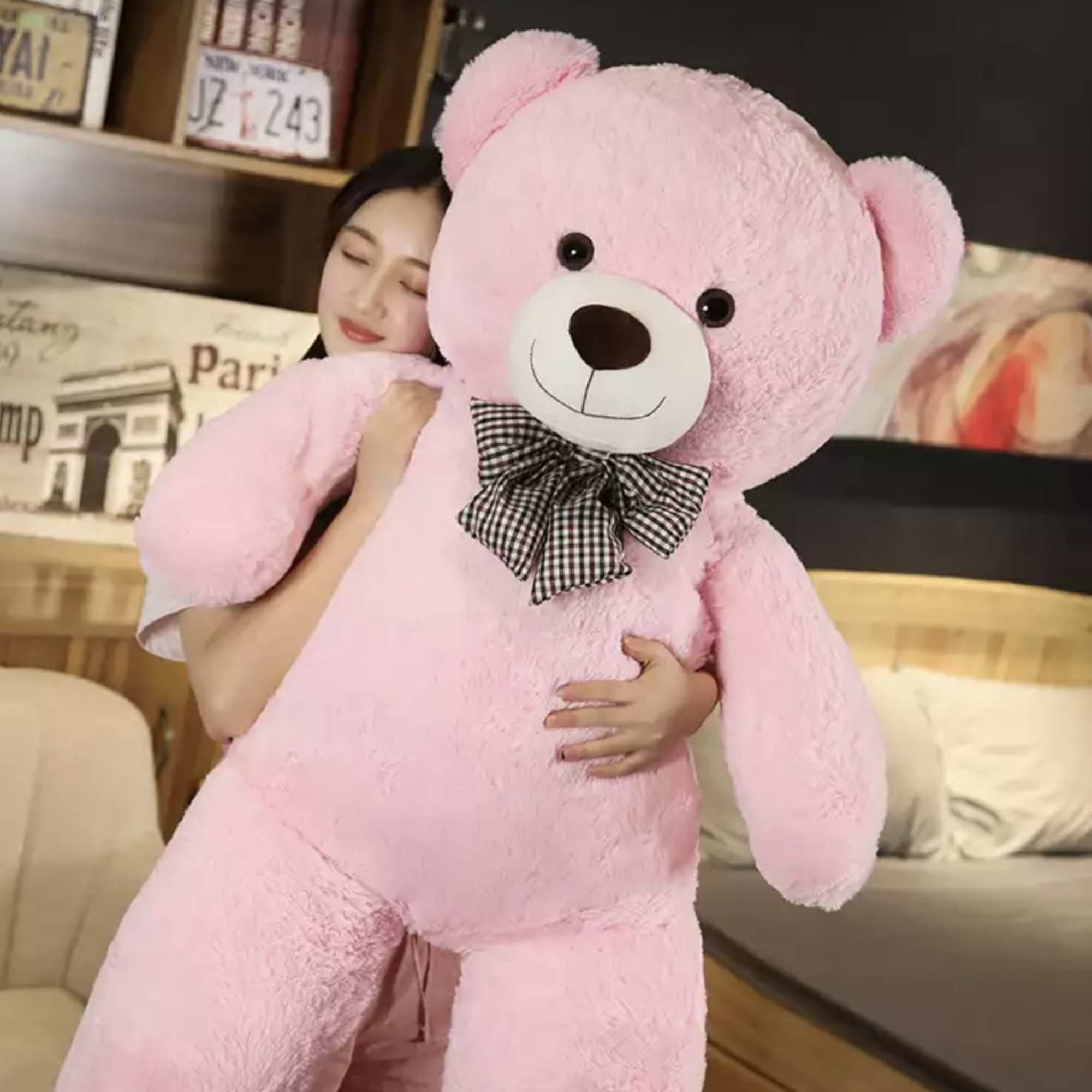 Woman holding a large pink teddy bear with a checkered bow