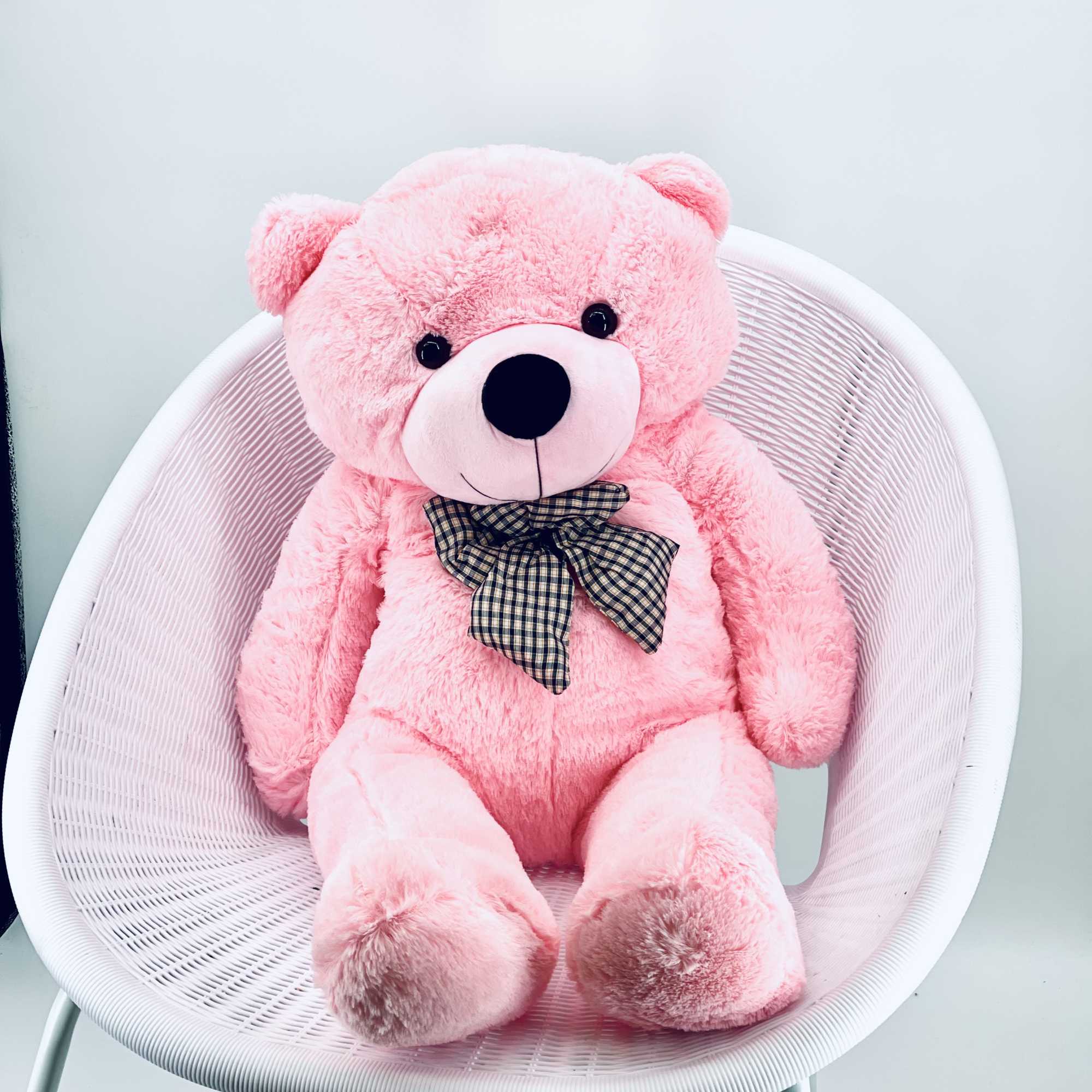 Pink teddy bear with a plaid bow sitting on a white chair