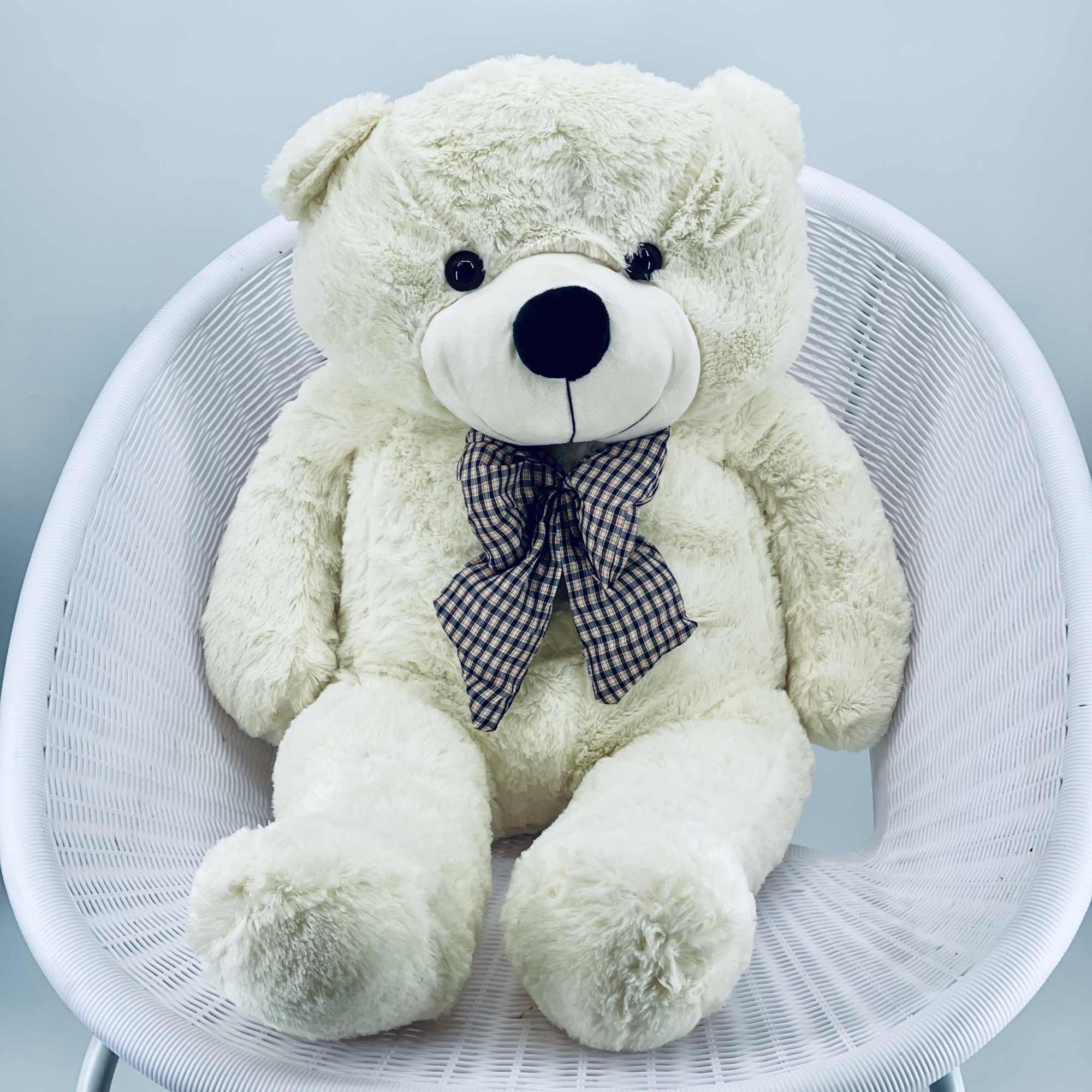 White teddy bear with a plaid bow sitting on a white chair