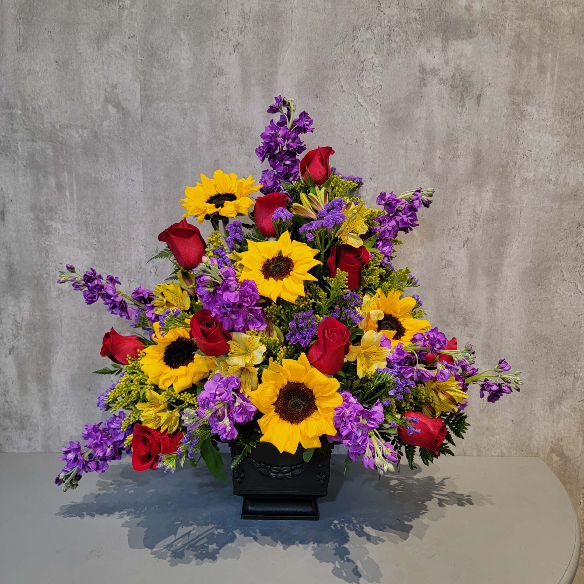 Sunflowers, red roses, and purple flowers in a black vase