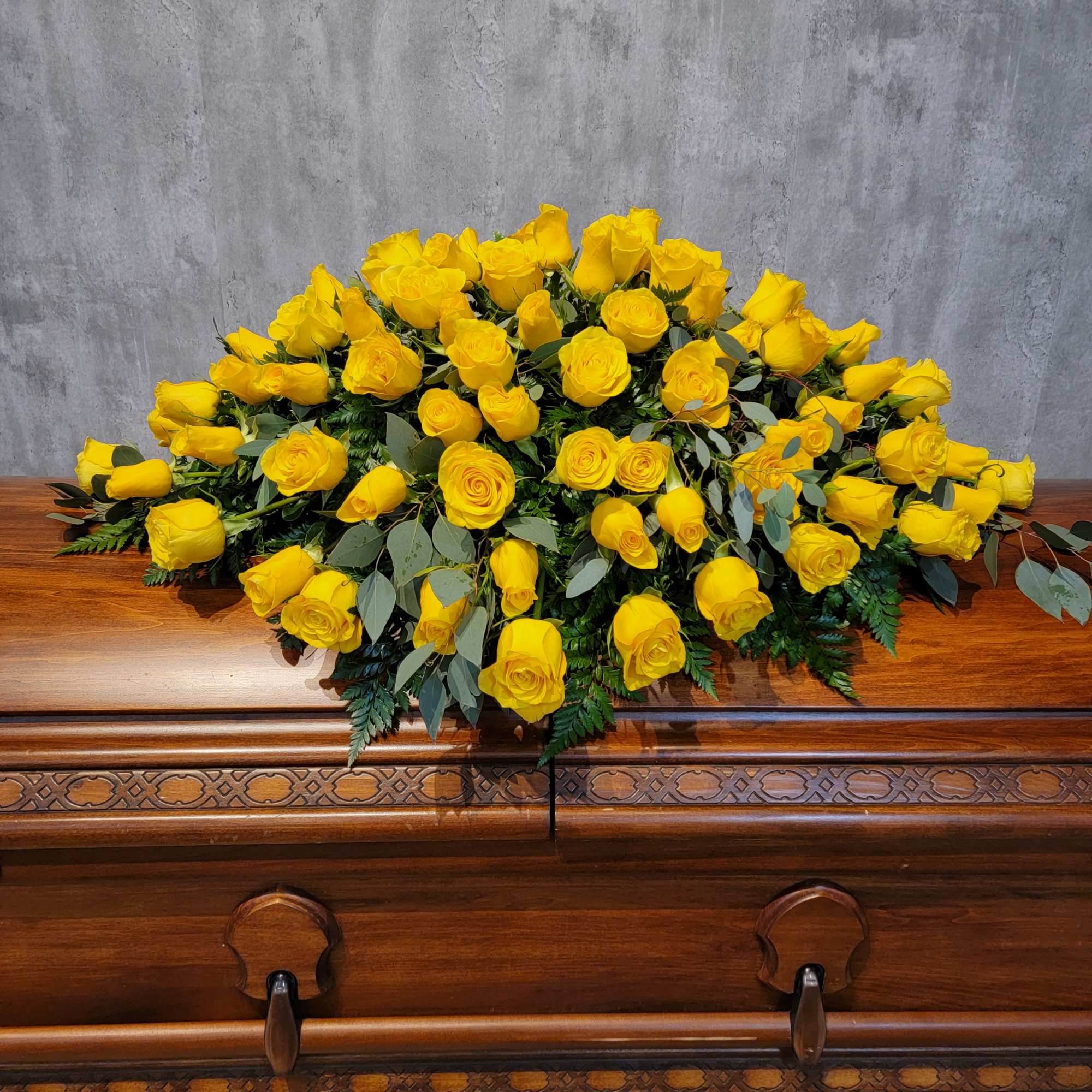Yellow rose casket spray with greenery on a wooden casket