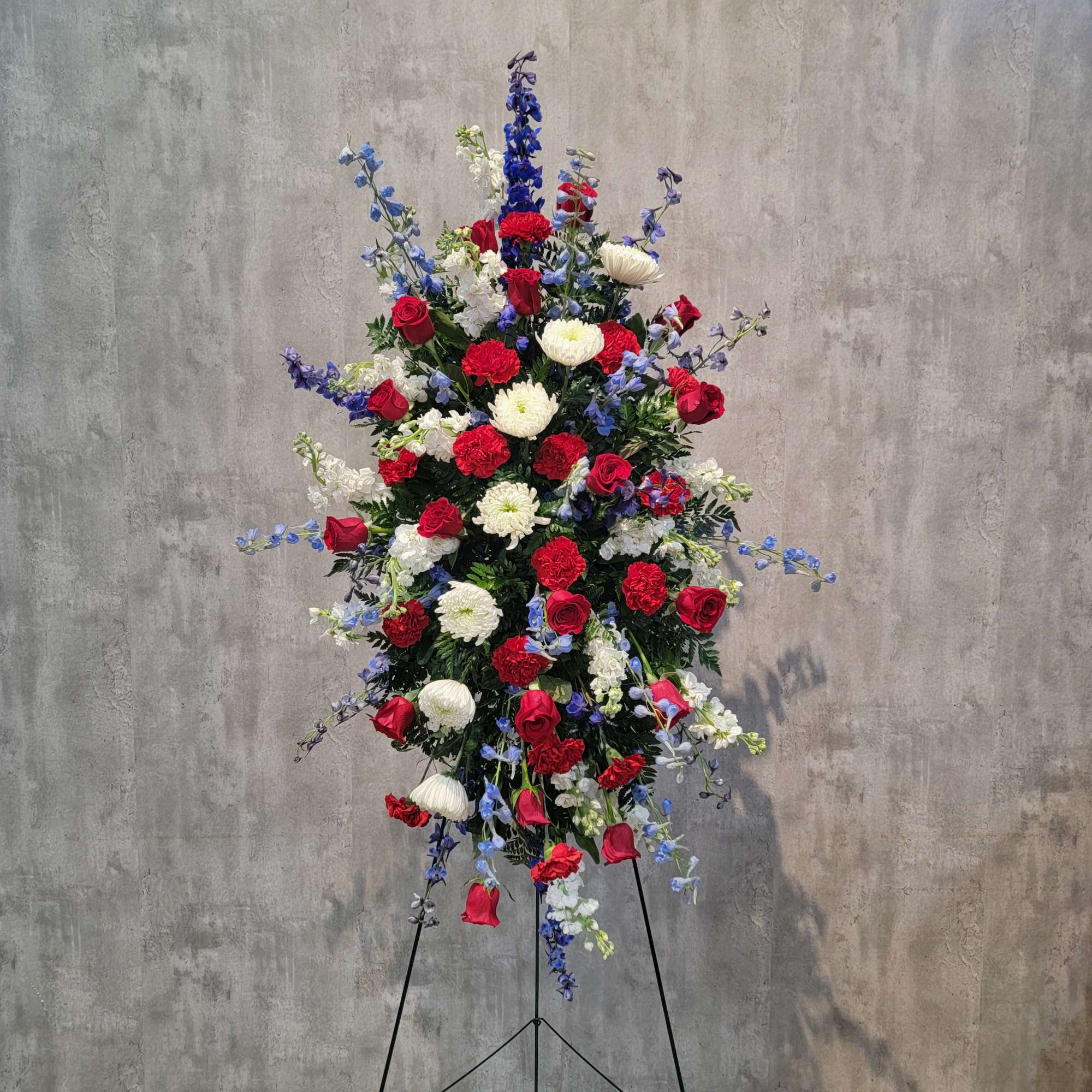 Tall standing floral spray with red, white, and blue flowers on a black easel