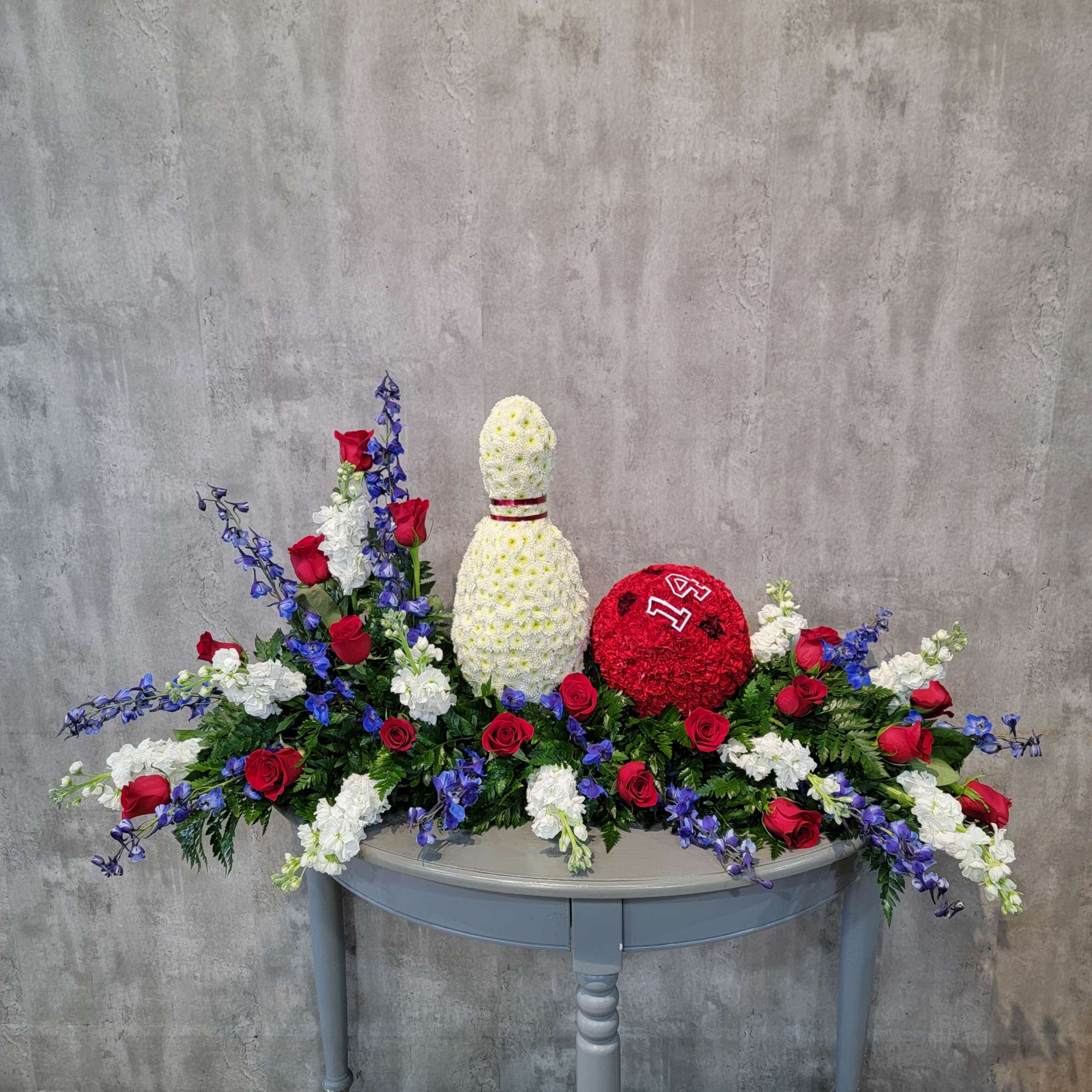 Large floral arrangement with red roses, white flowers, and blue delphinium around a white centerpiece.