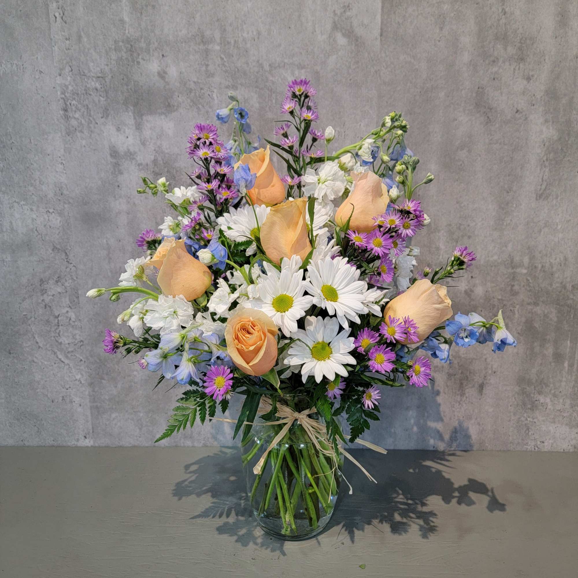 Mixed bouquet of peach roses, white daisies, and purple flowers in a glass vase