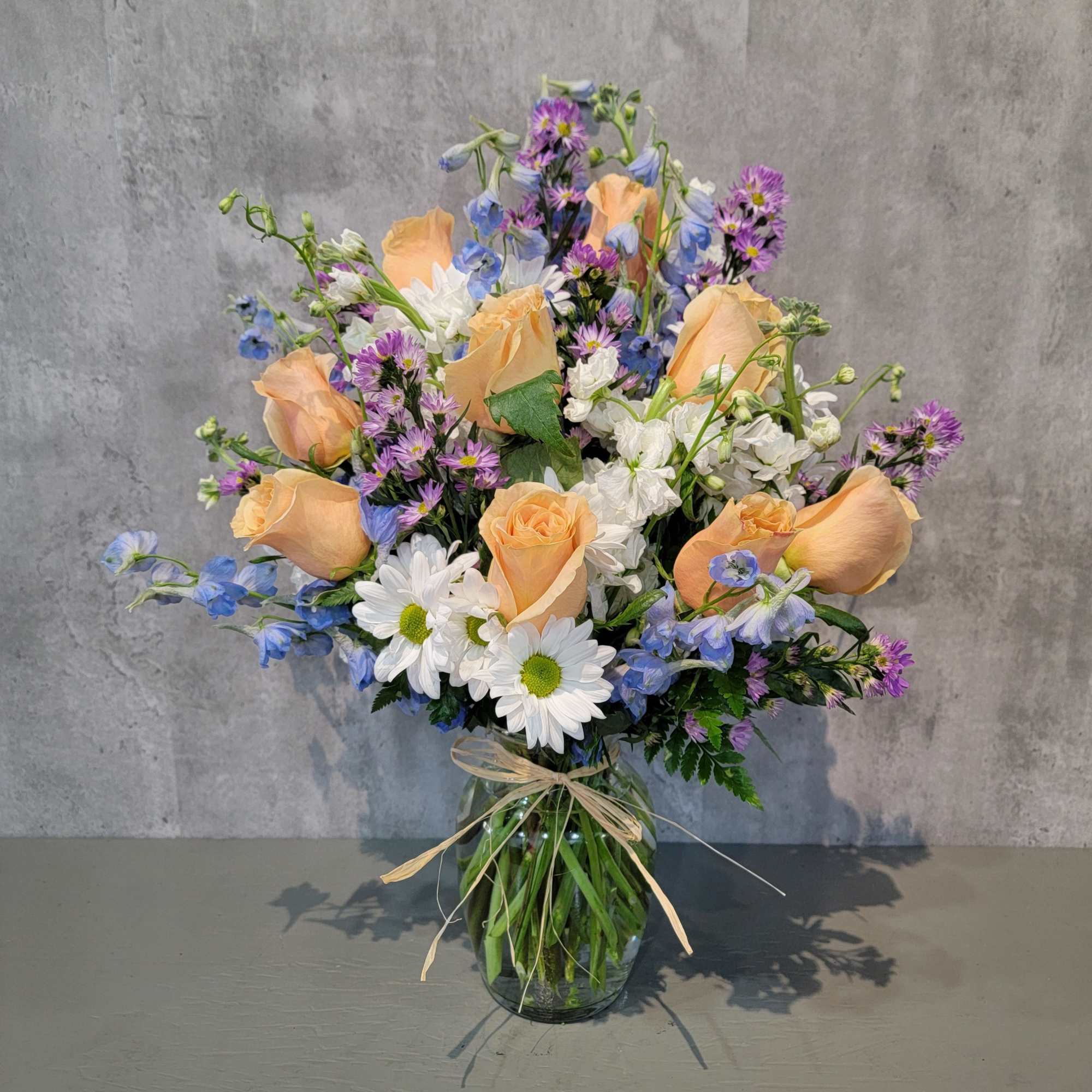 Peach roses, white daisies, and blue-purple flowers in a glass vase