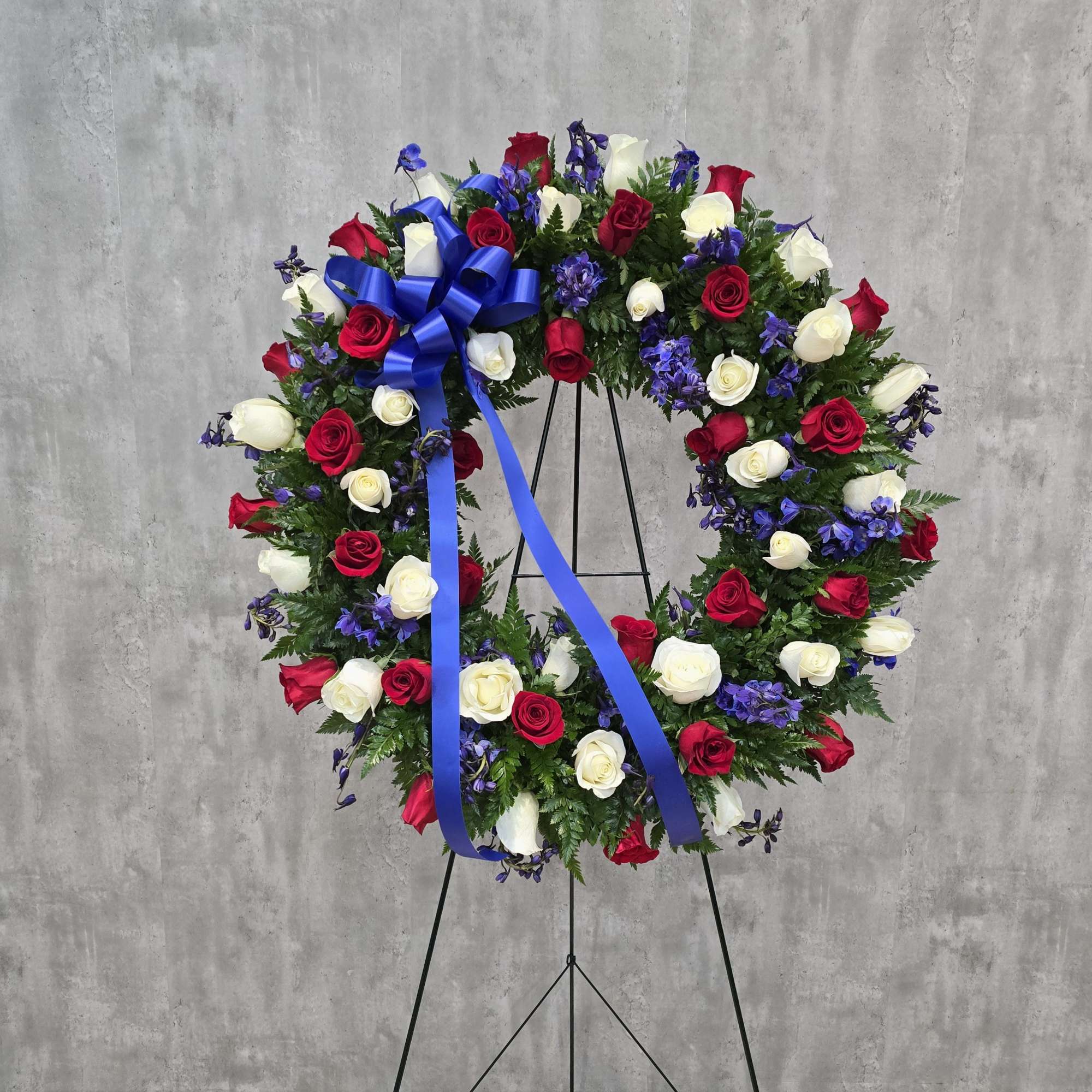 Circular wreath of red and white roses with blue ribbon on a stand