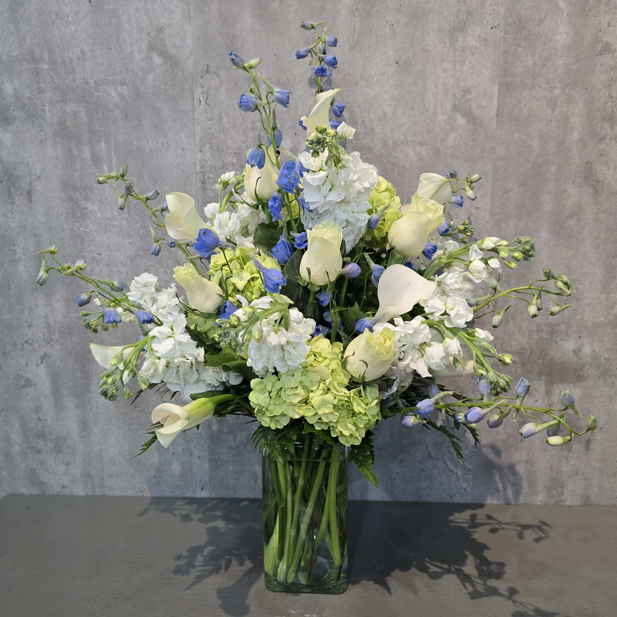 White calla lilies and blue flowers in a tall glass vase