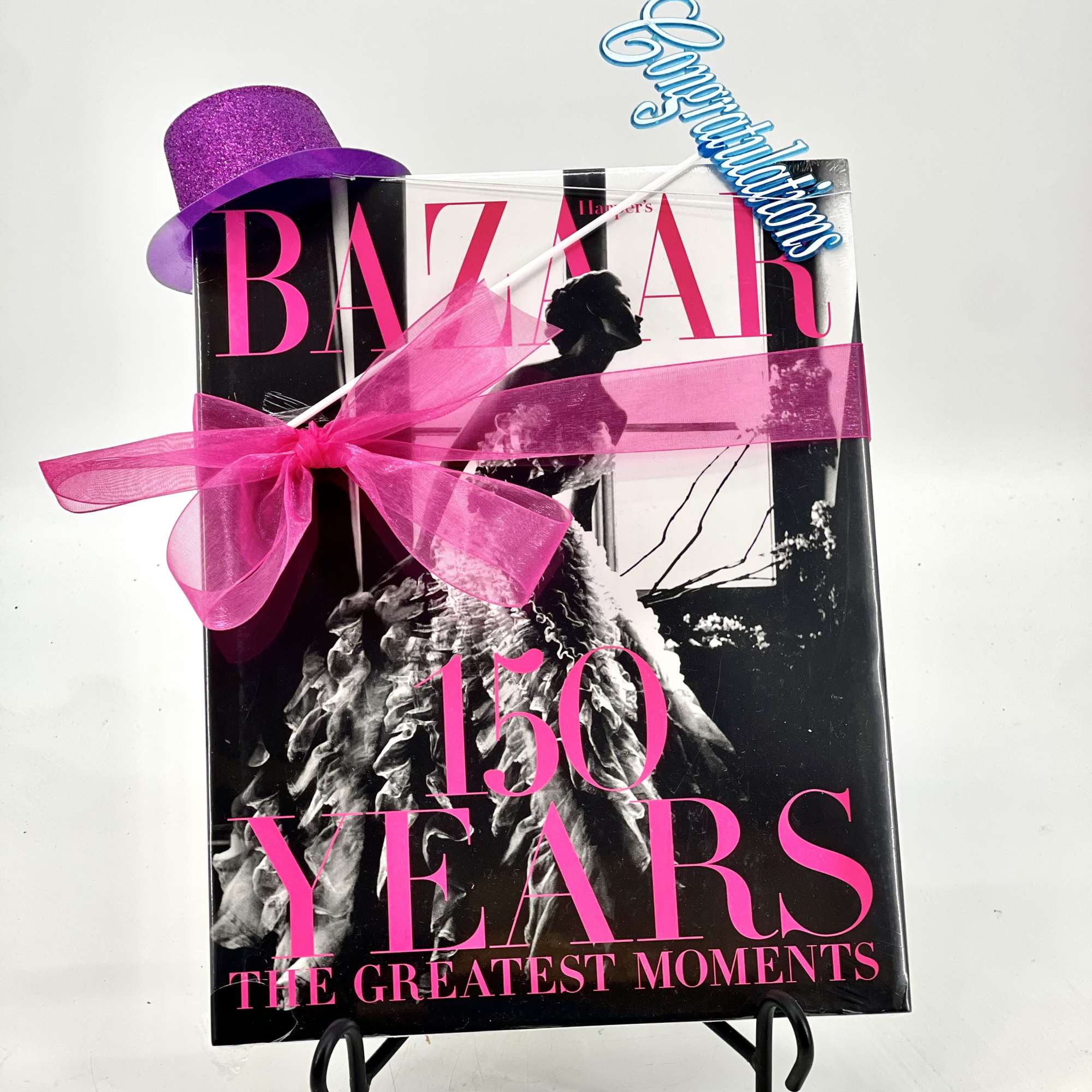 Gift-wrapped Harper's Bazaar 150 Years book with a purple hat and pink ribbon
