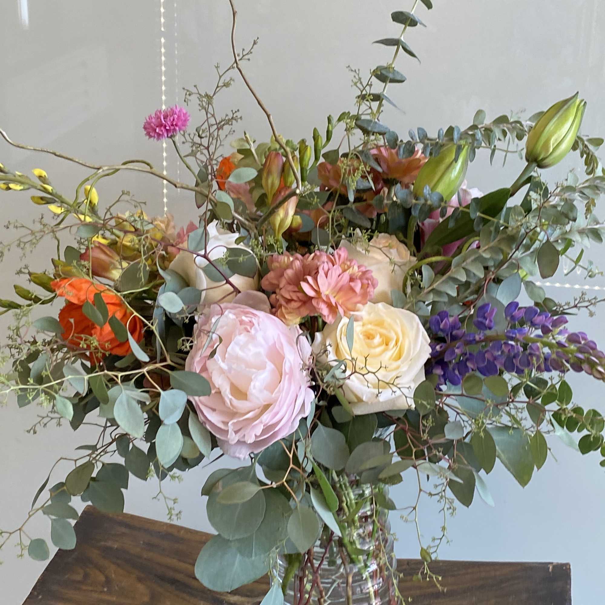 Mixed bouquet of roses, lilies, and purple flowers in a glass vase