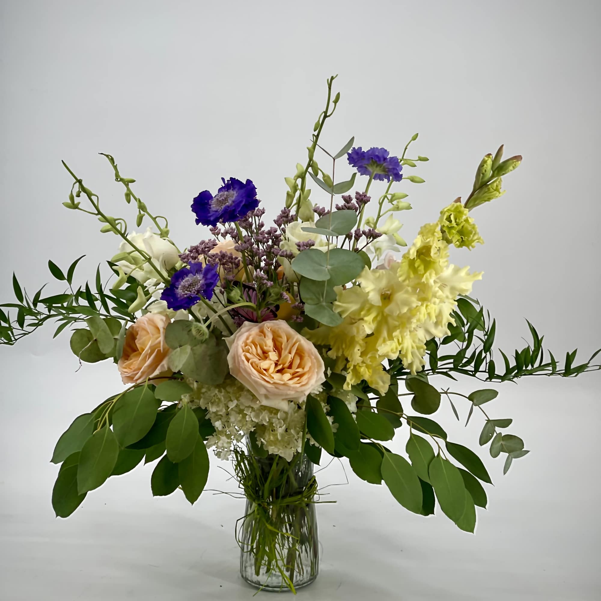 Mixed bouquet in a clear glass vase with peach roses and purple blooms