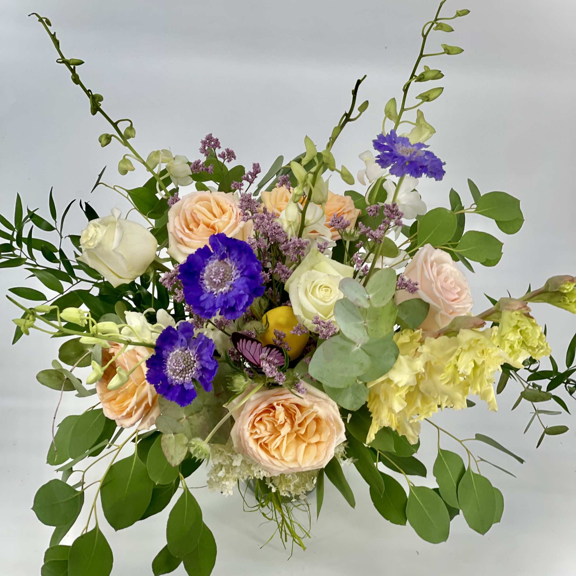 Peach and white roses with purple blooms in a loose bouquet
