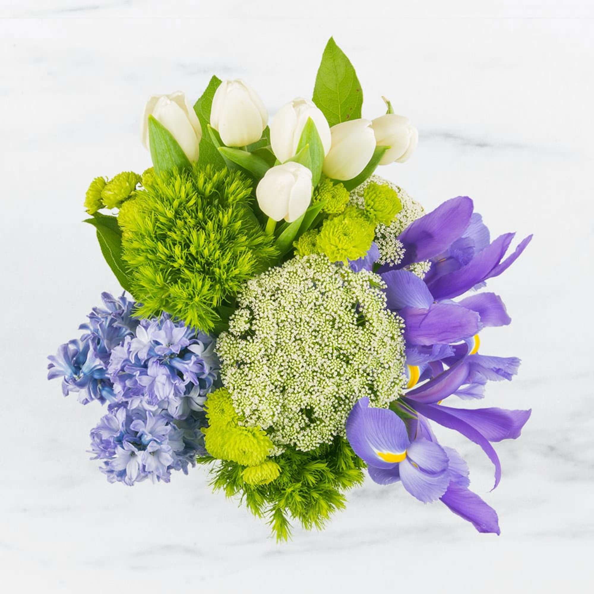 This arrangement includes green dianthus, blue iris, white tulips, hyacinths, and other