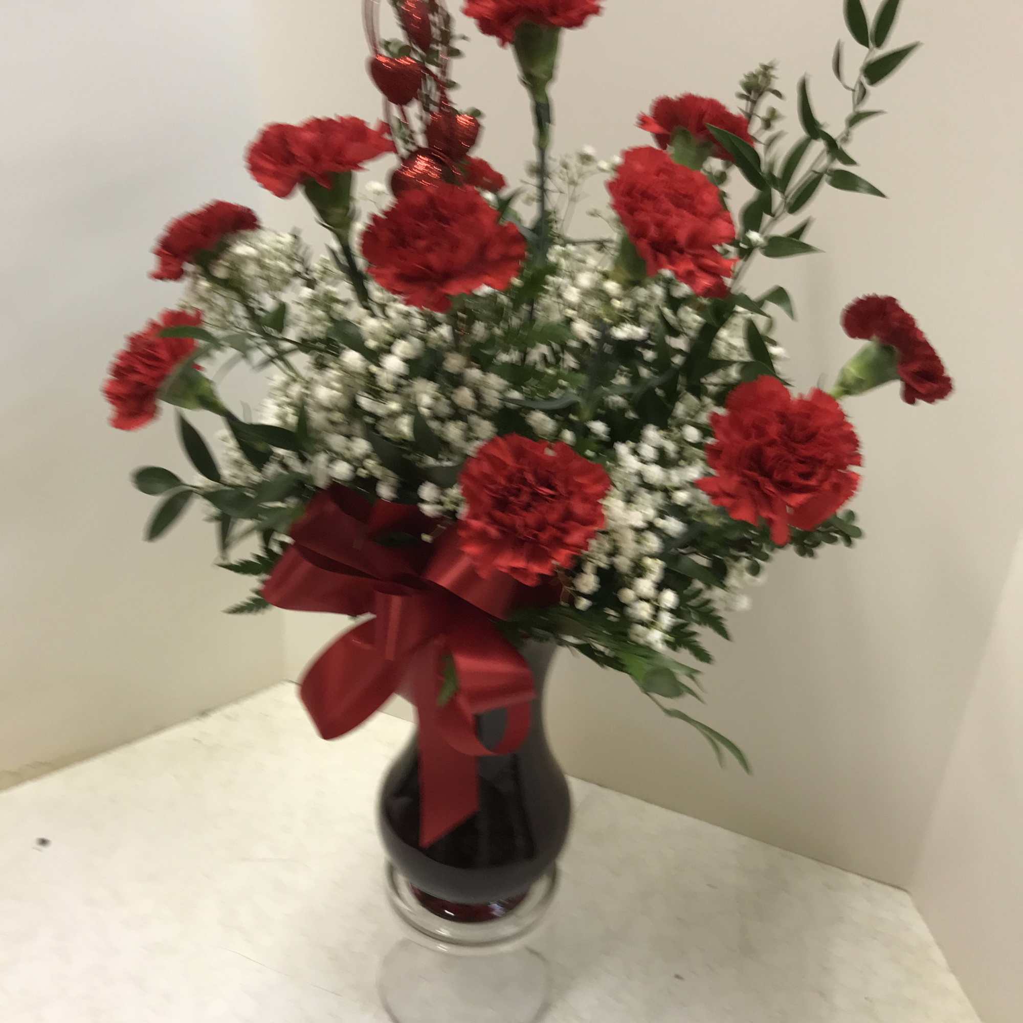 Red carnations in a glass vase with baby's breath and a red ribbon