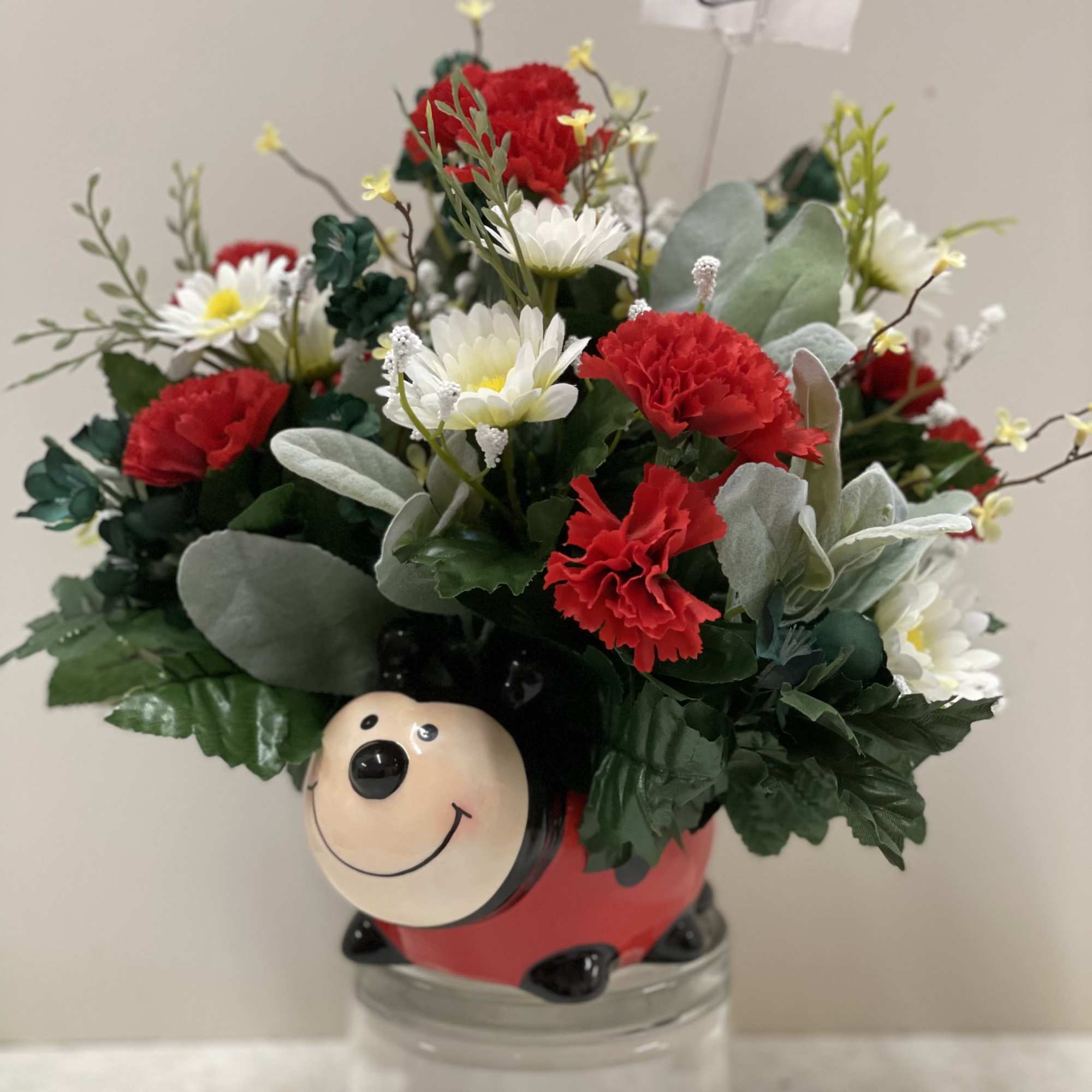 Bouquet of red carnations and white daisies in a ladybug container