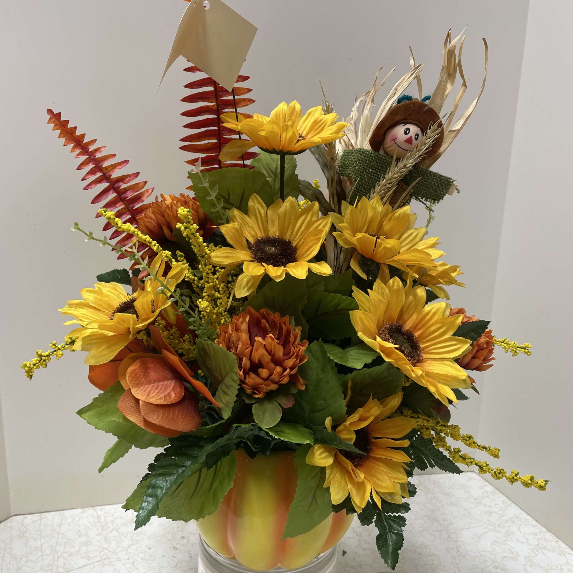 Sunflower arrangement in a clear glass vase with a small scarecrow pick
