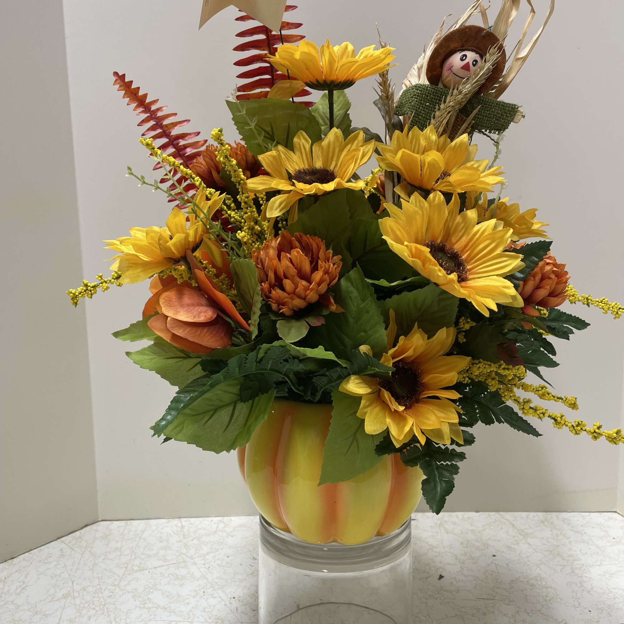 Sunflower arrangement in a pumpkin-shaped vase with a scarecrow pick