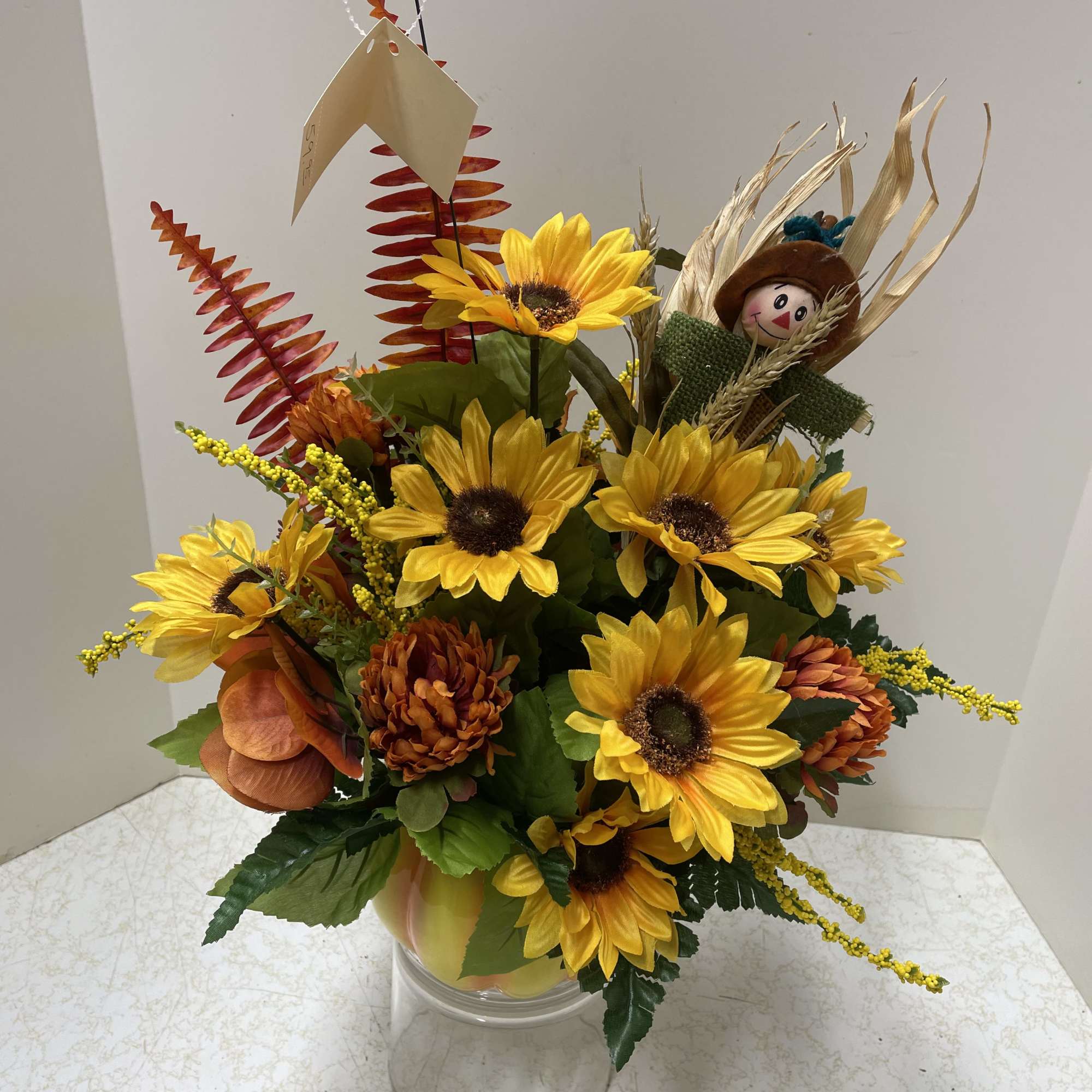 Sunflower arrangement in a clear vase with autumn accents and a small scarecrow figure