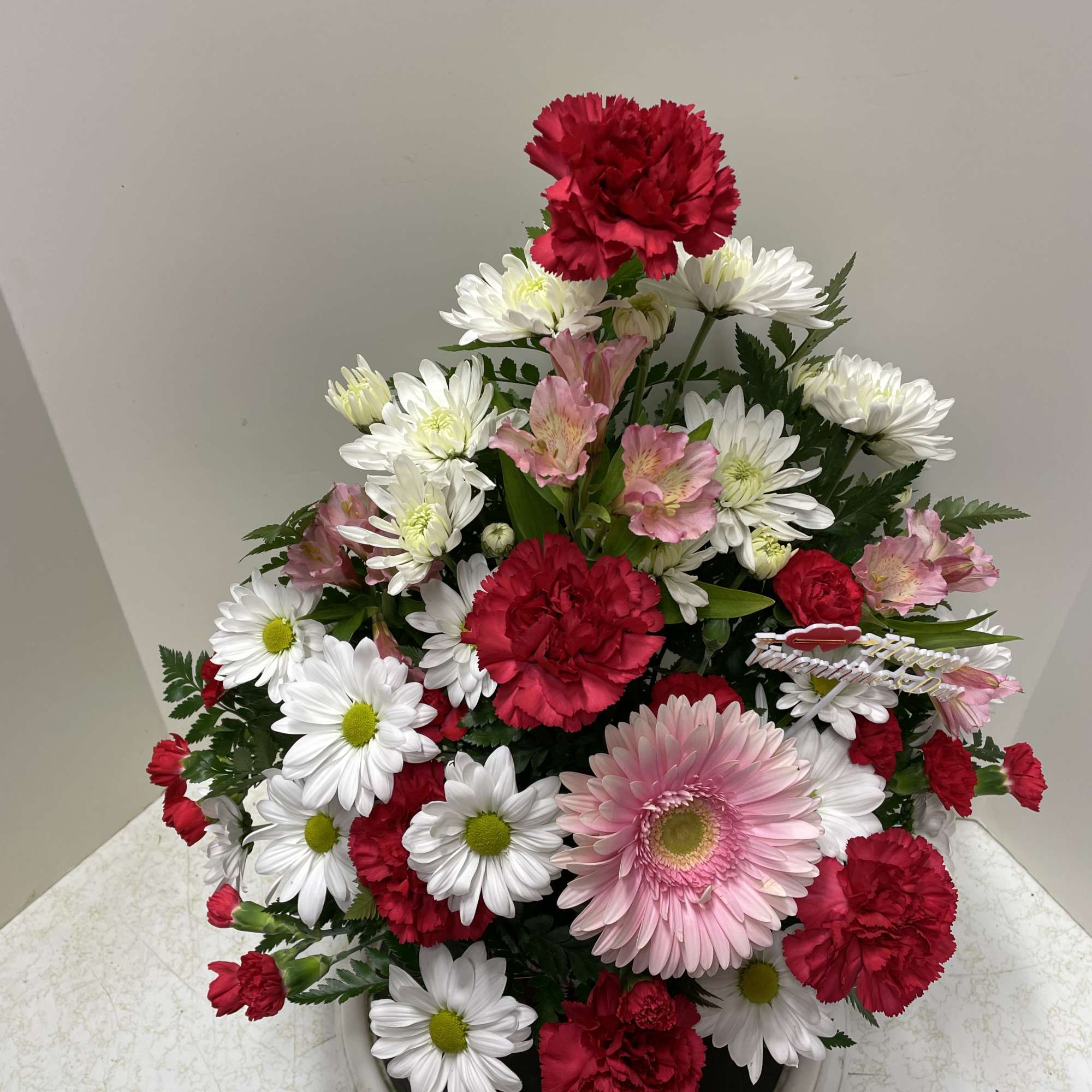 Mixed bouquet of red carnations, white daisies, and pink gerbera in a vase