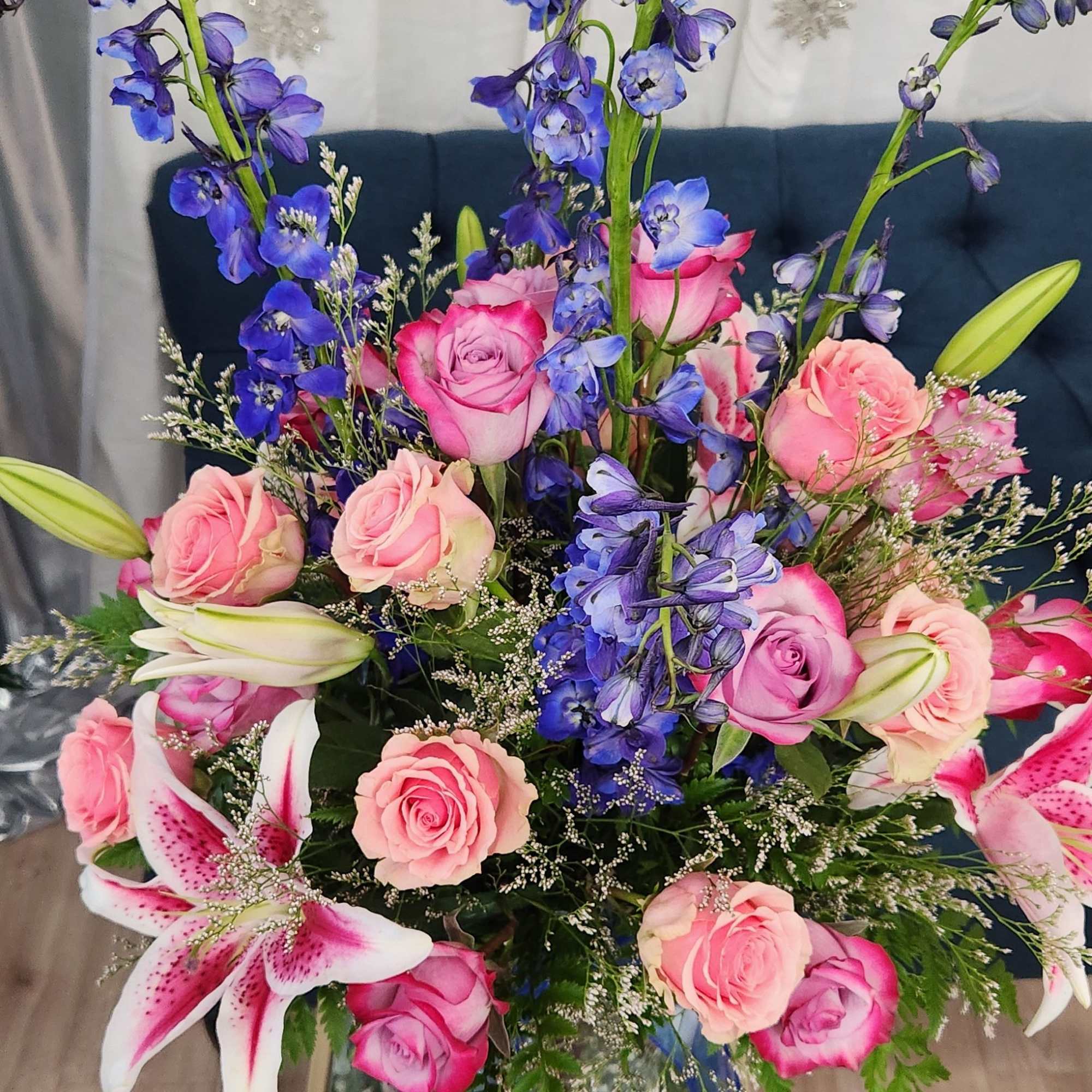 Tall bouquet of pink roses, blue delphinium, and white lilies in a vase