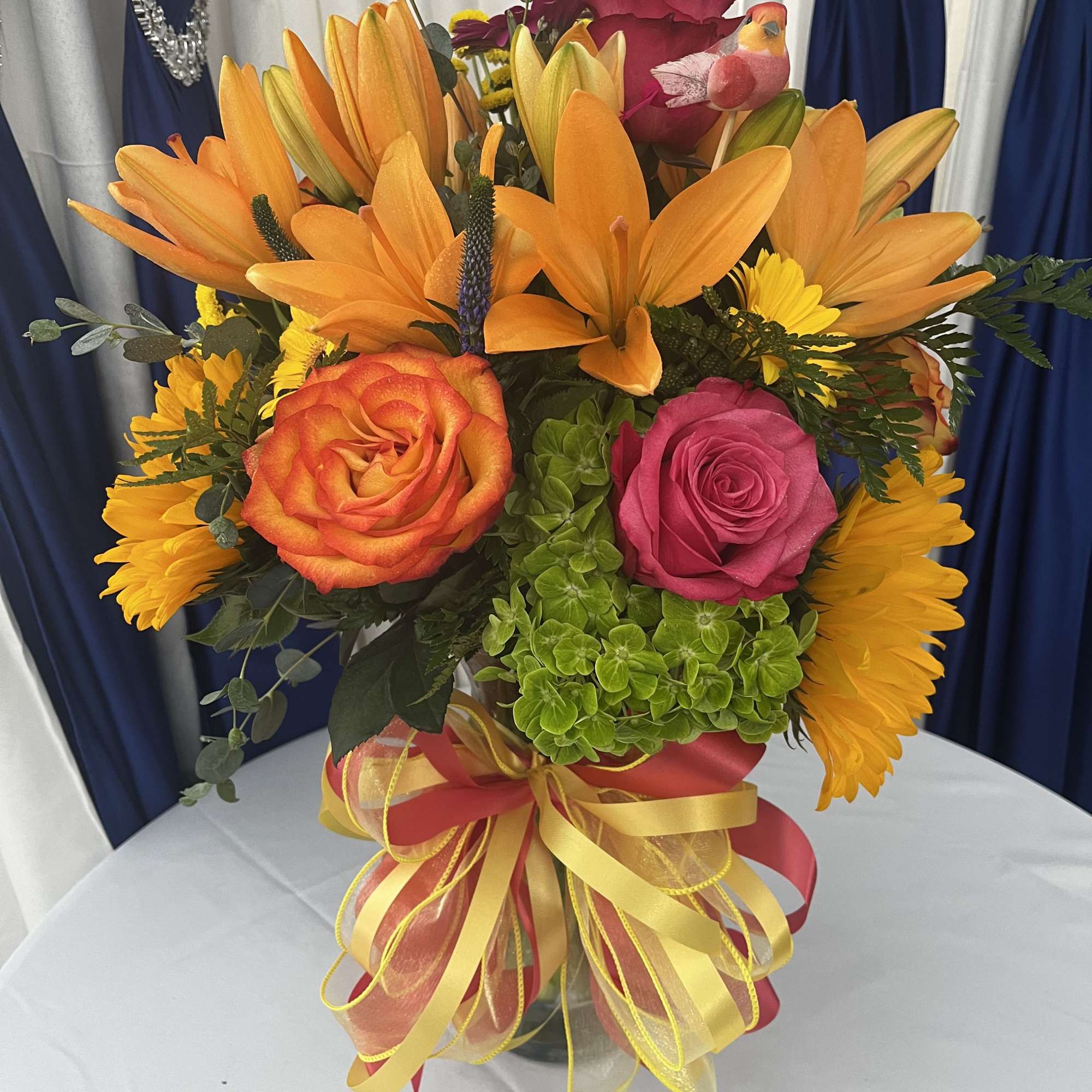 Bright bouquet of orange lilies, roses, and yellow daisies in a glass vase