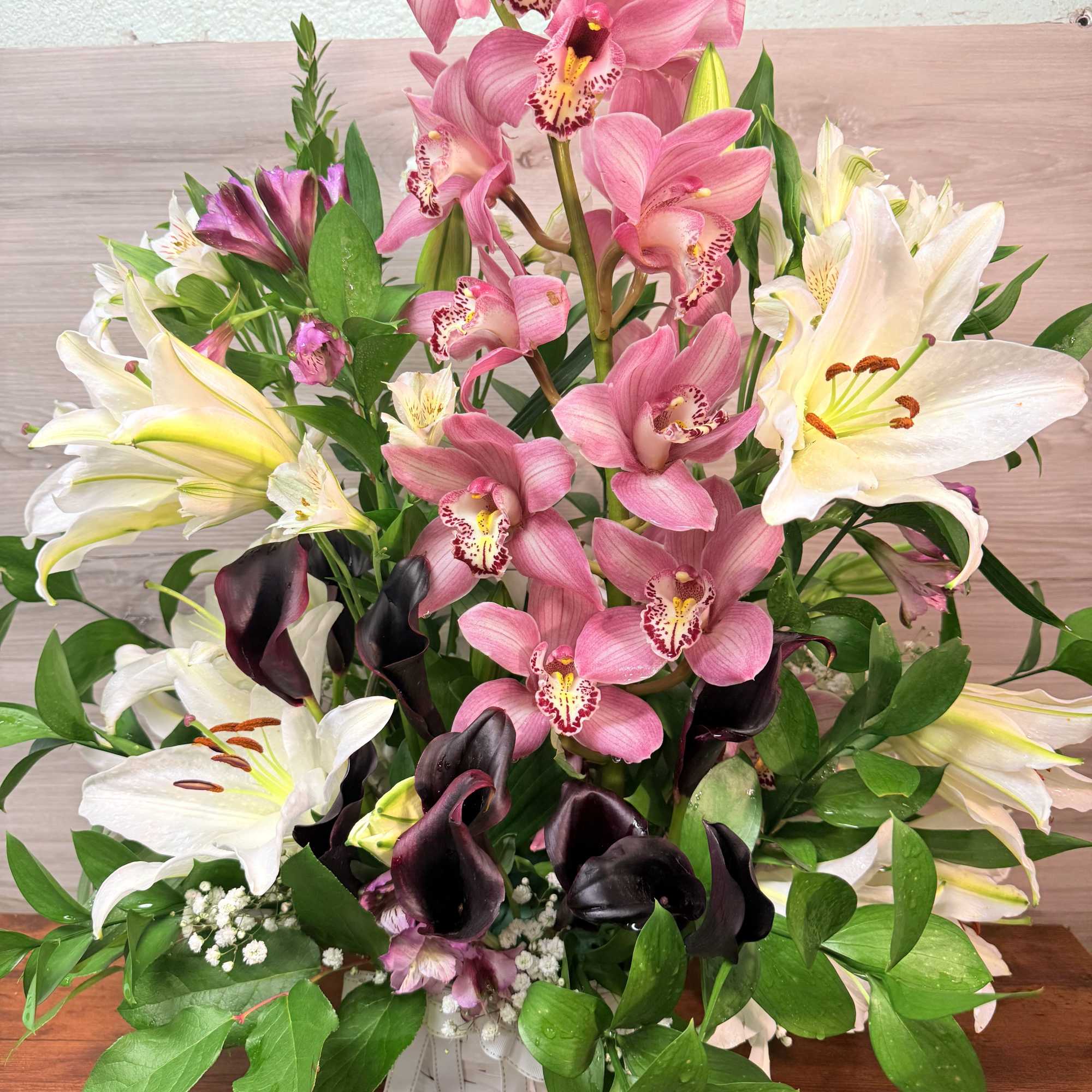 Mixed bouquet with pink orchids, white lilies, and dark calla lilies in a vase