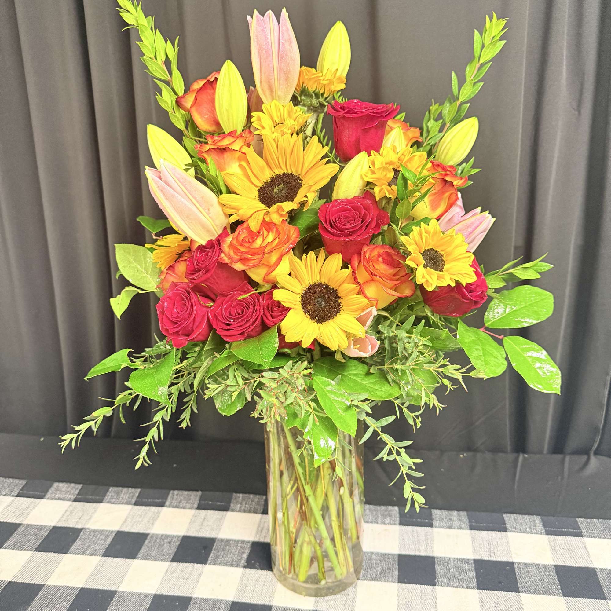 Bouquet of red roses, sunflowers, and pink lilies in a glass vase