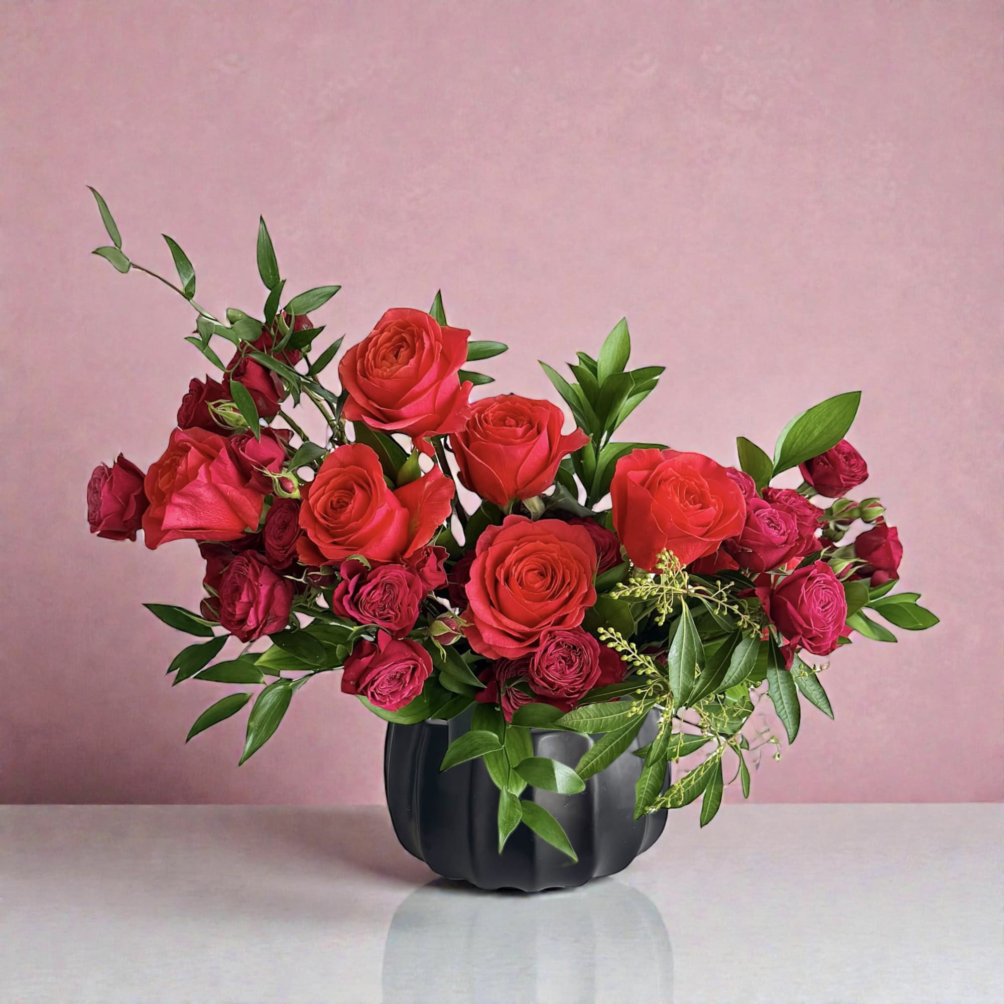 Red roses arranged in a black vase with green foliage