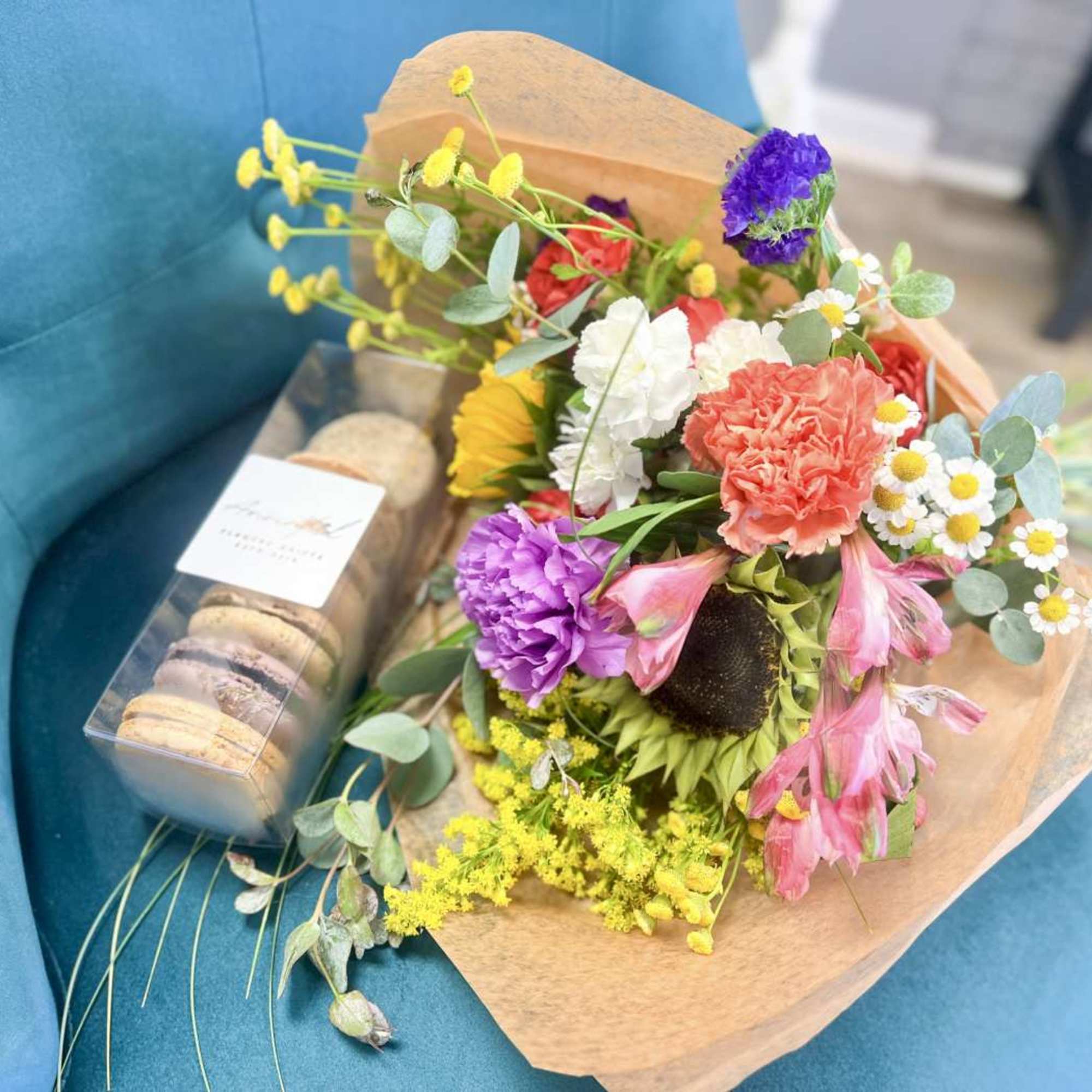 Bright mixed bouquet with carnations, daisies and other blooms paired with a box of macarons.