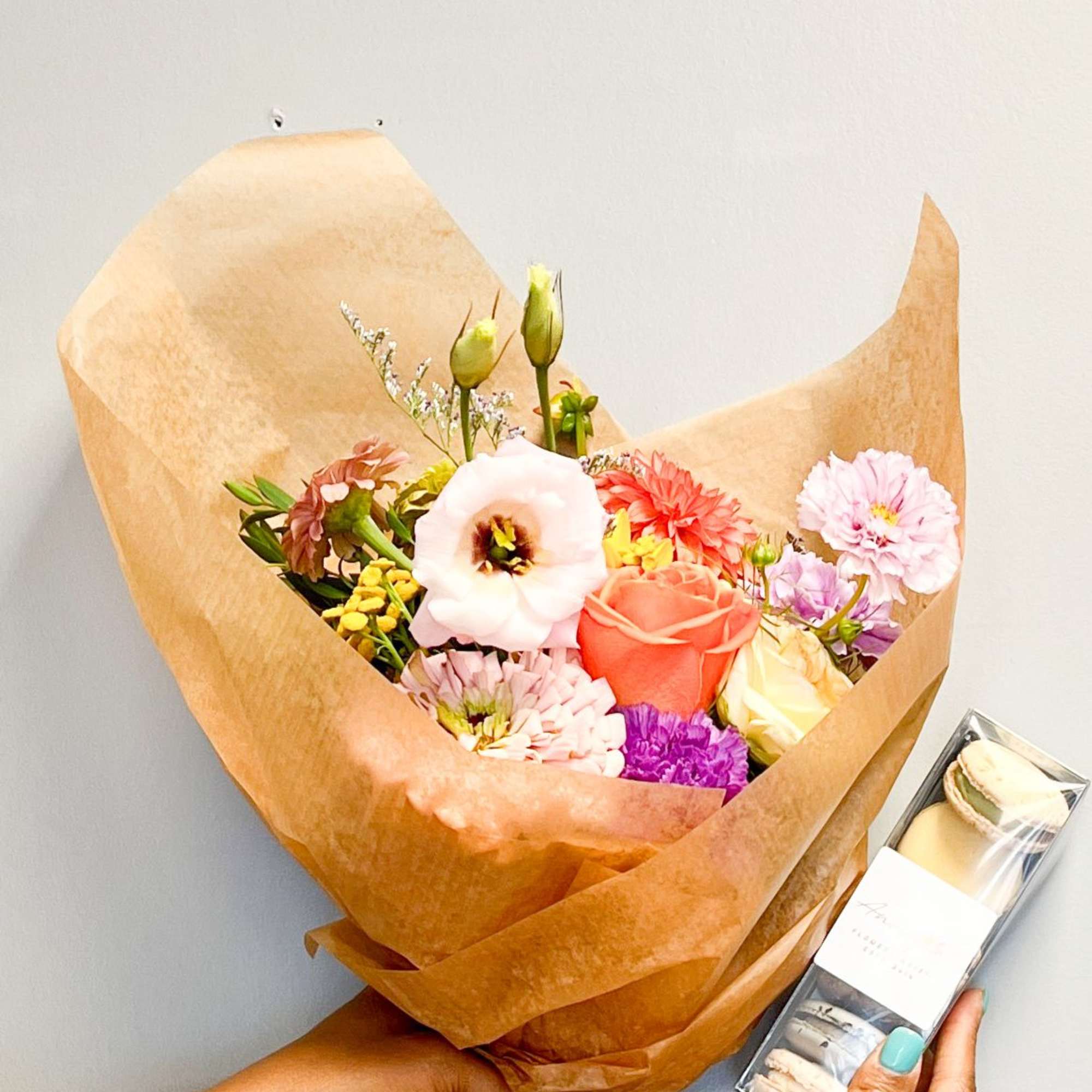 Hand-tied mixed flower bouquet in kraft paper wrapping with a box of macarons.