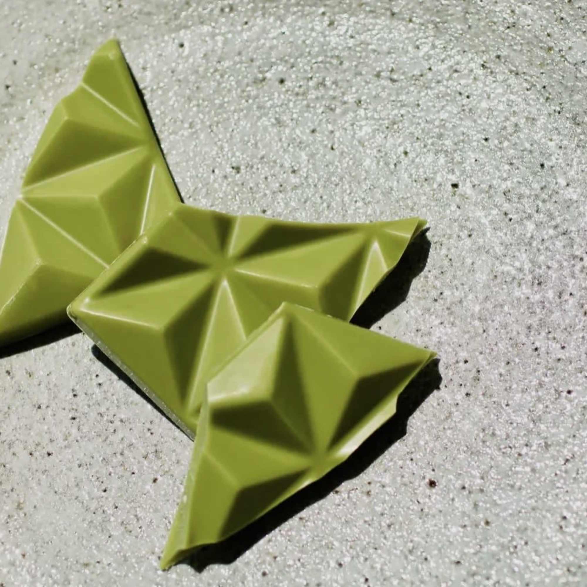 Three green geometric chocolate pieces on a speckled surface