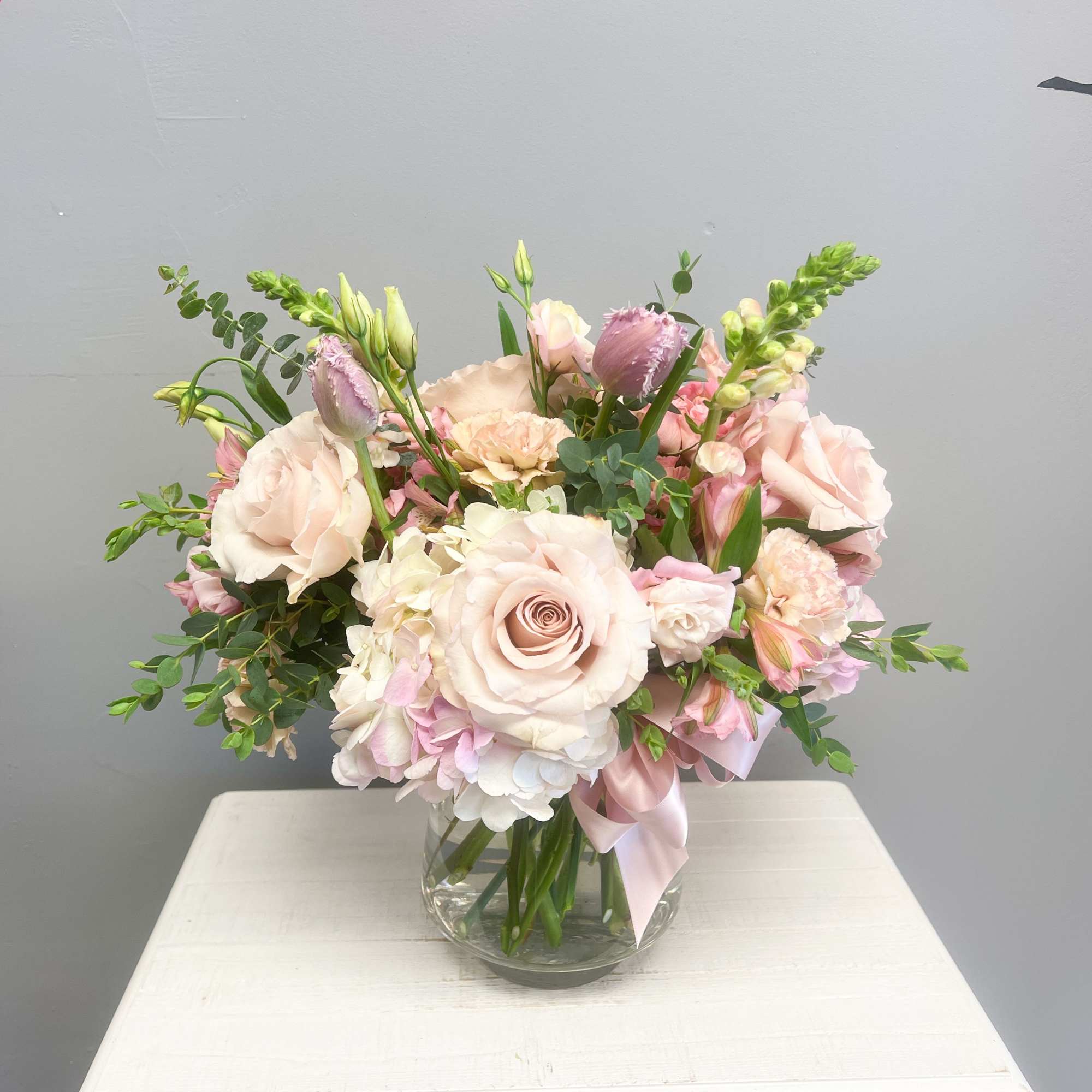 Round arrangement of blush roses and white hydrangea in a clear glass vase on a white table
