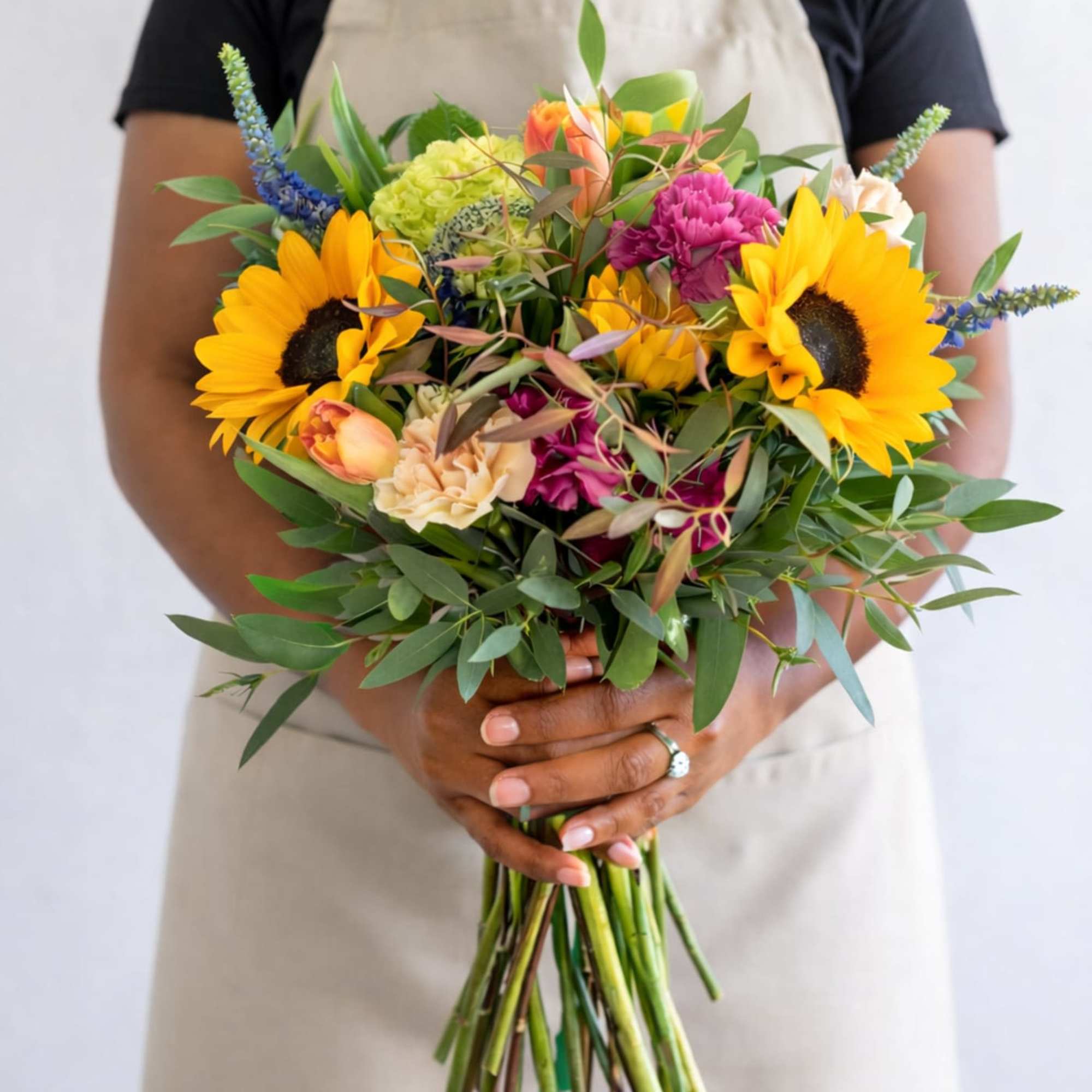 Florist holding a hand-tied bouquet with yellow sunflowers and mixed bright blooms.