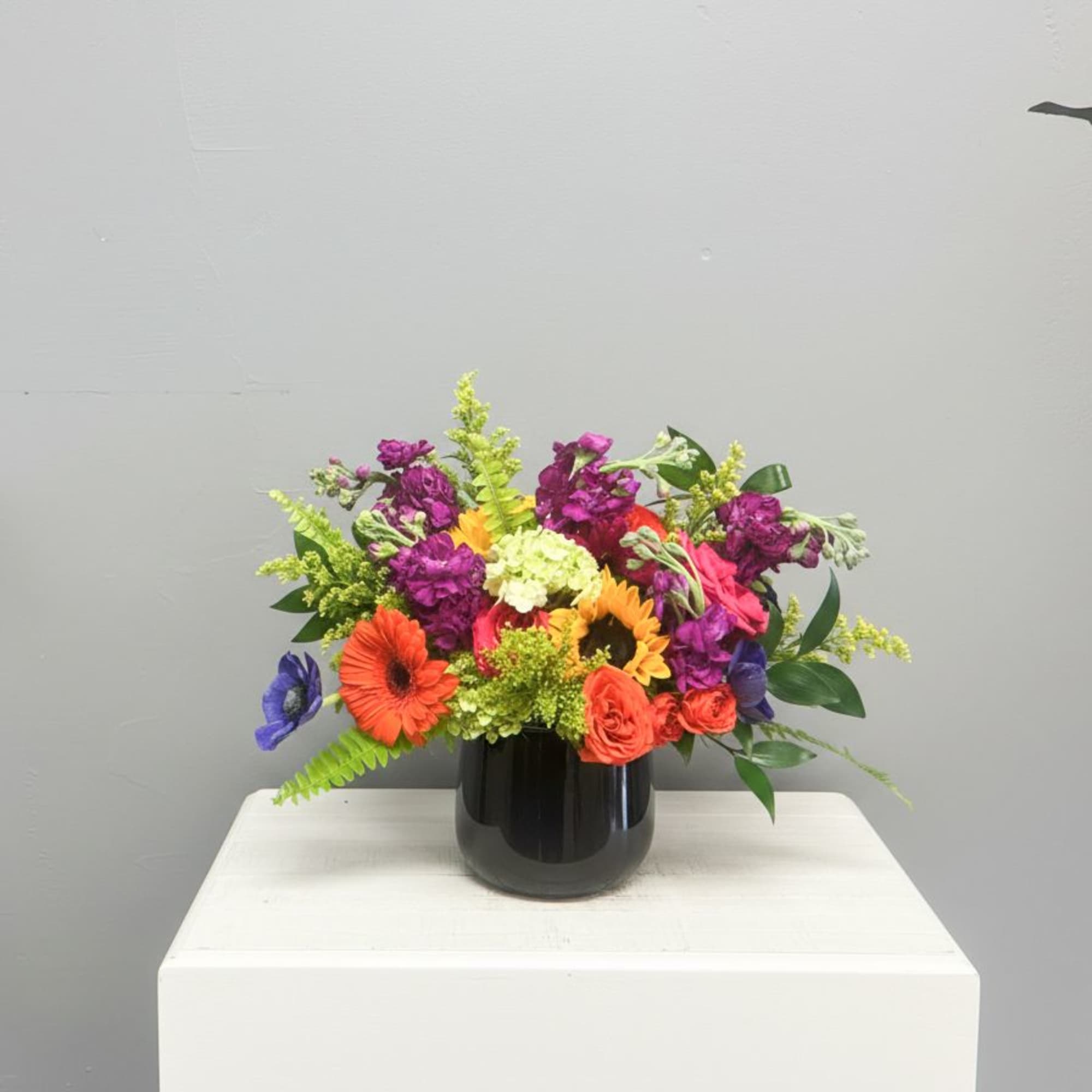 Low multicolor flower arrangement with gerbera daisies, roses, and stock in a black vase