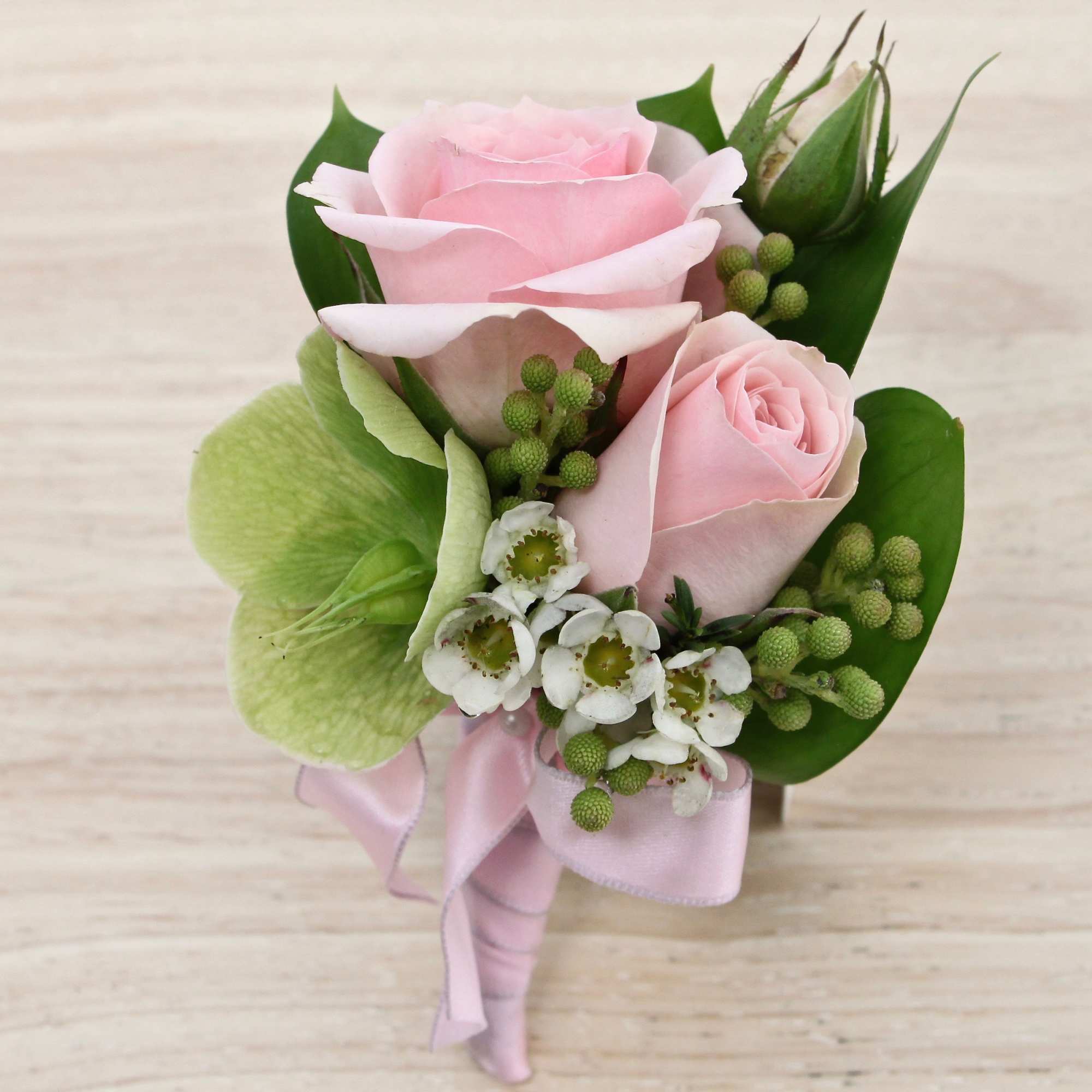 Pink rose corsage with green orchid, white filler flowers, and berries tied with a pink satin ribbon.