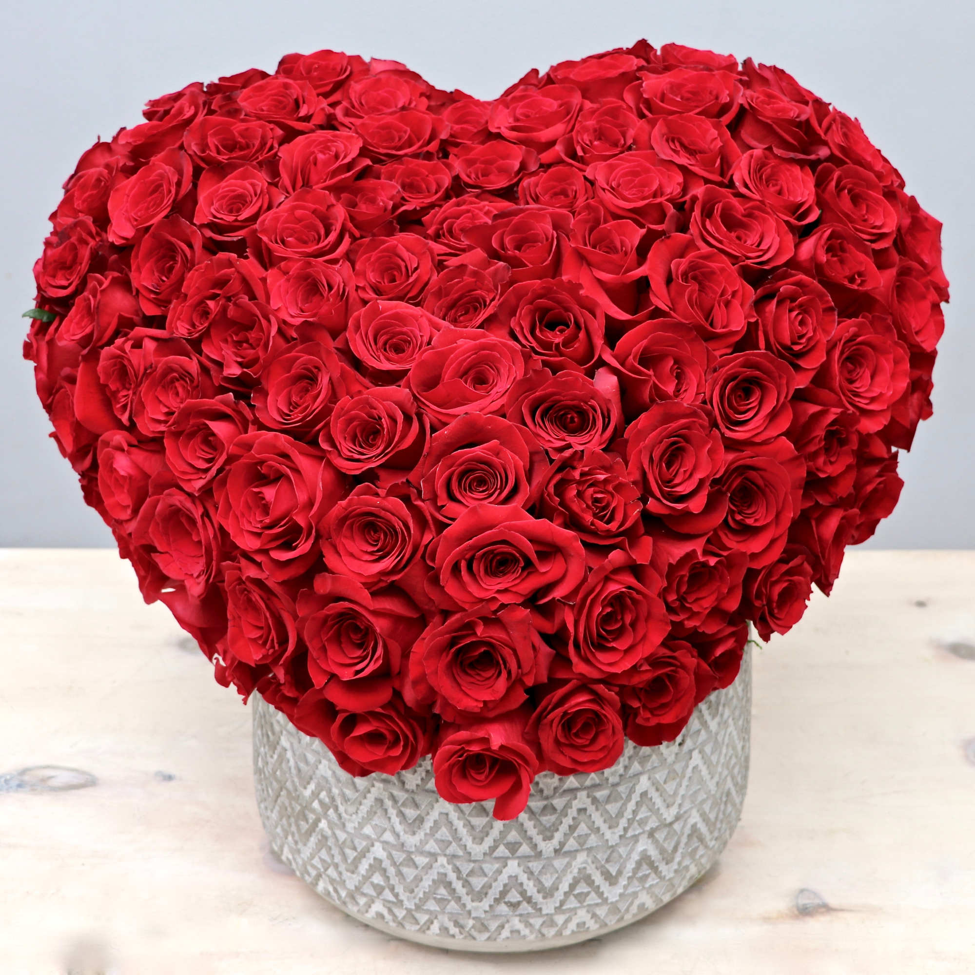 Heart-shaped arrangement of red roses in a patterned white ceramic pot