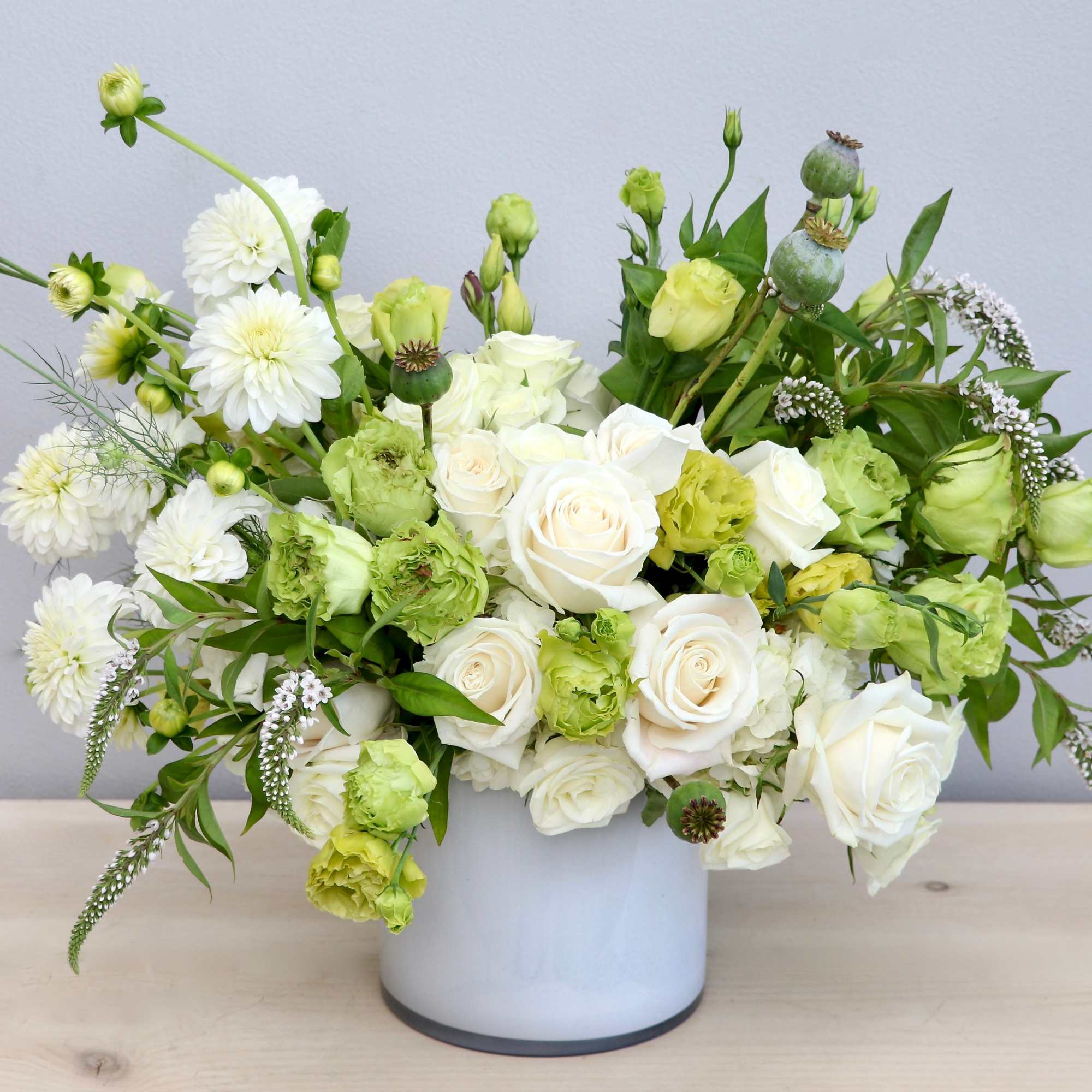 Low white and green flower arrangement with roses and round blooms in a white cylinder vase