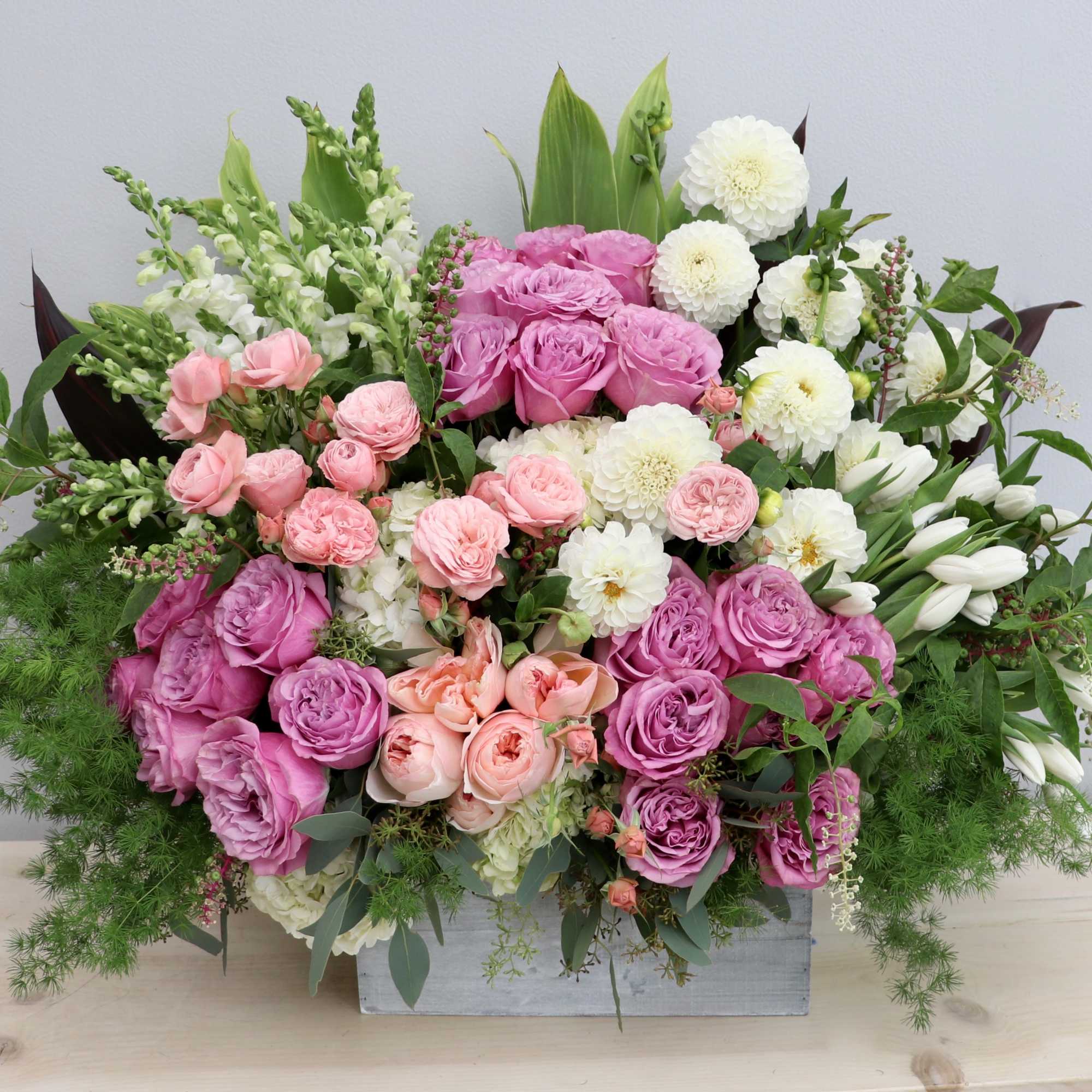 Low wooden box arrangement with pink roses, white blooms, and white tulips in a full, rounded design