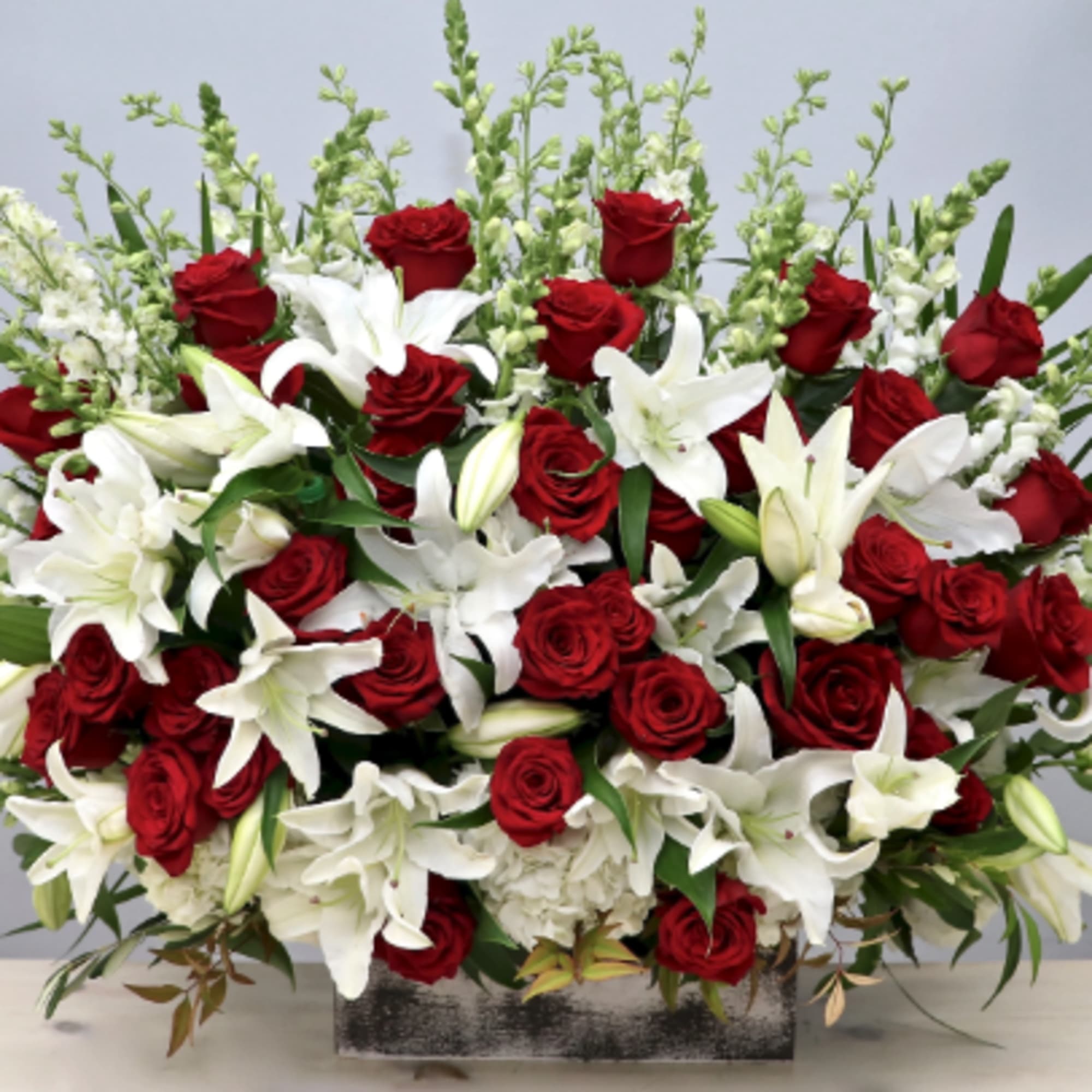 Large red rose and white lily arrangement with snapdragons in a rustic rectangular container