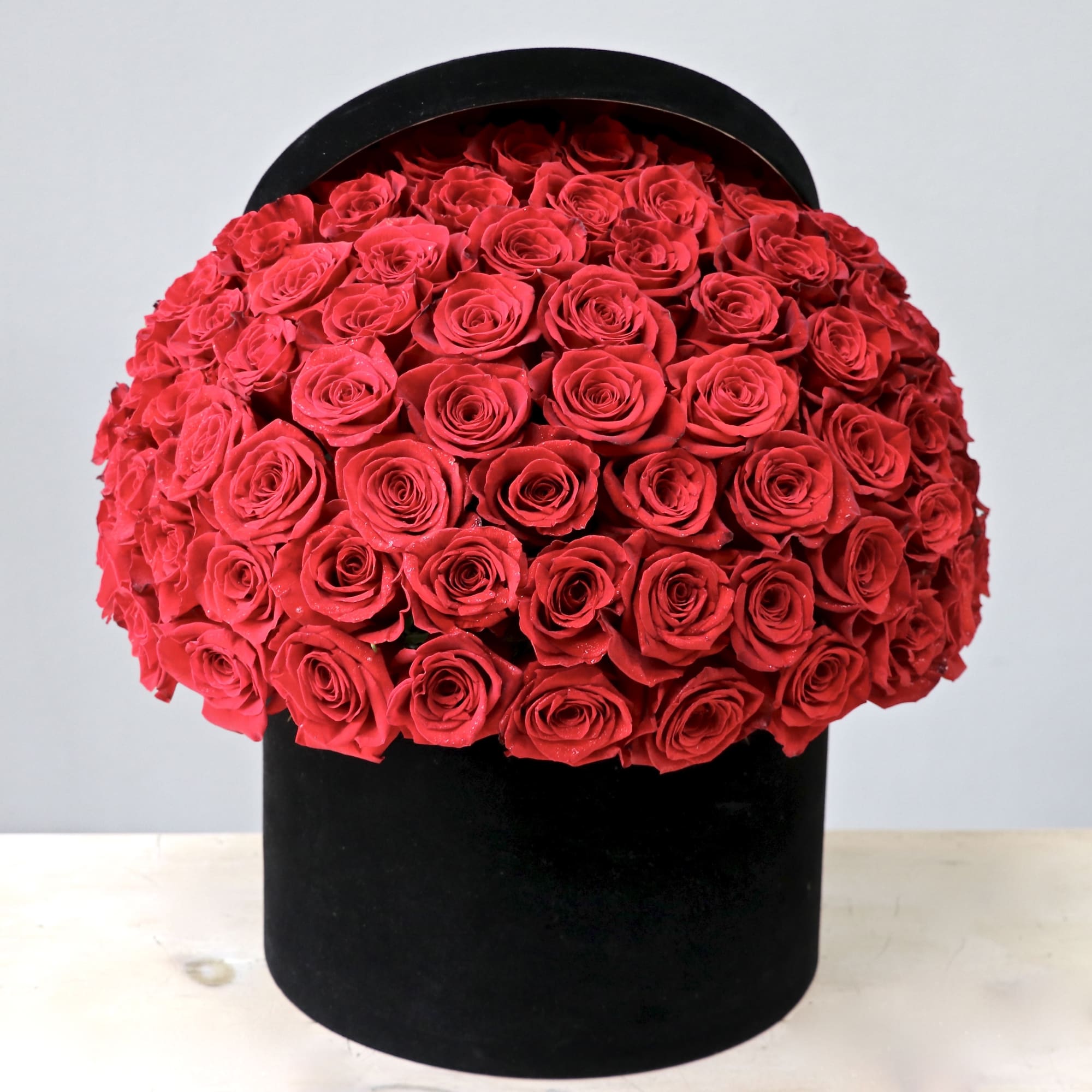 Large dome of red roses arranged tightly in a black hatbox-style container