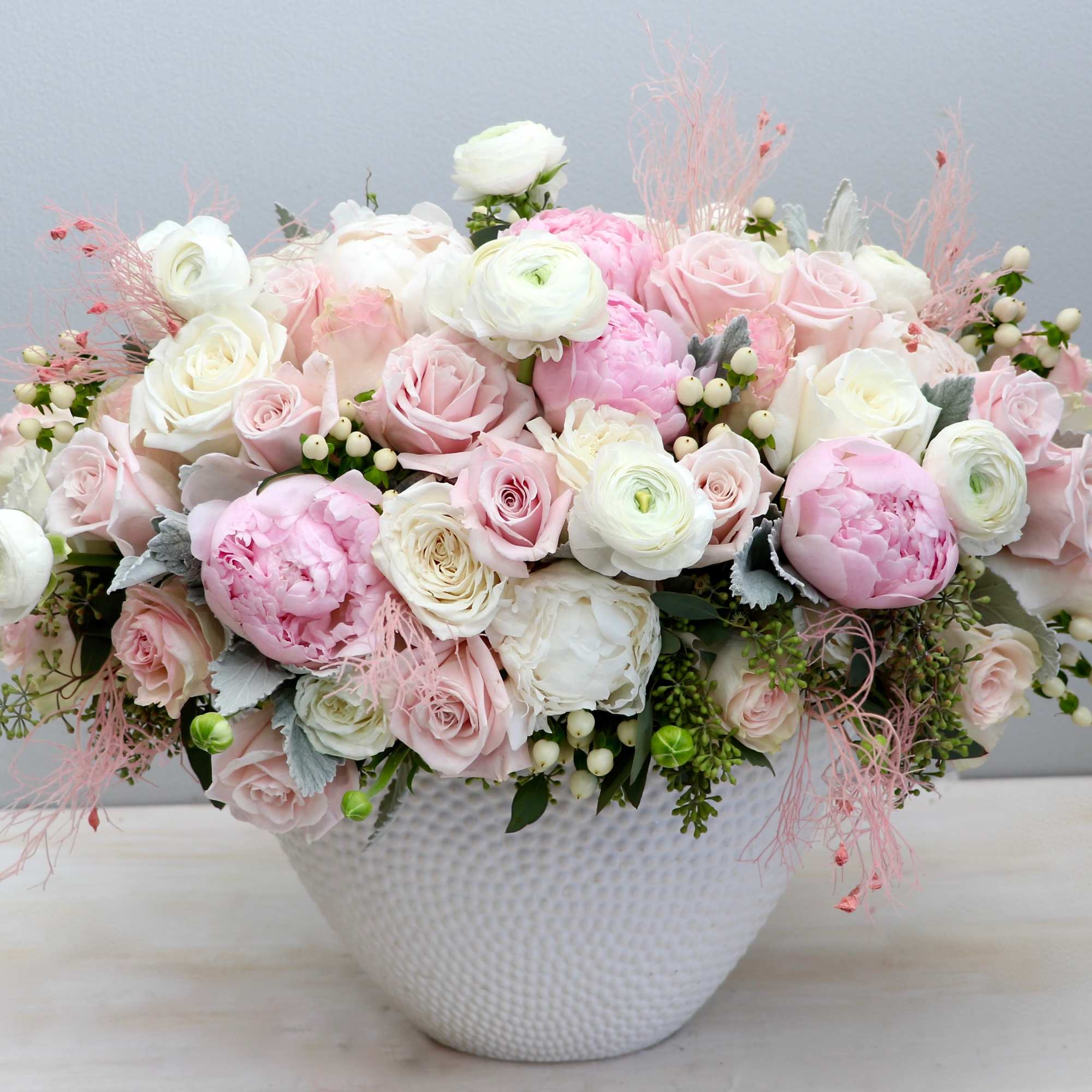Low white bowl filled with lush pink and white roses, peonies, and ranunculus.