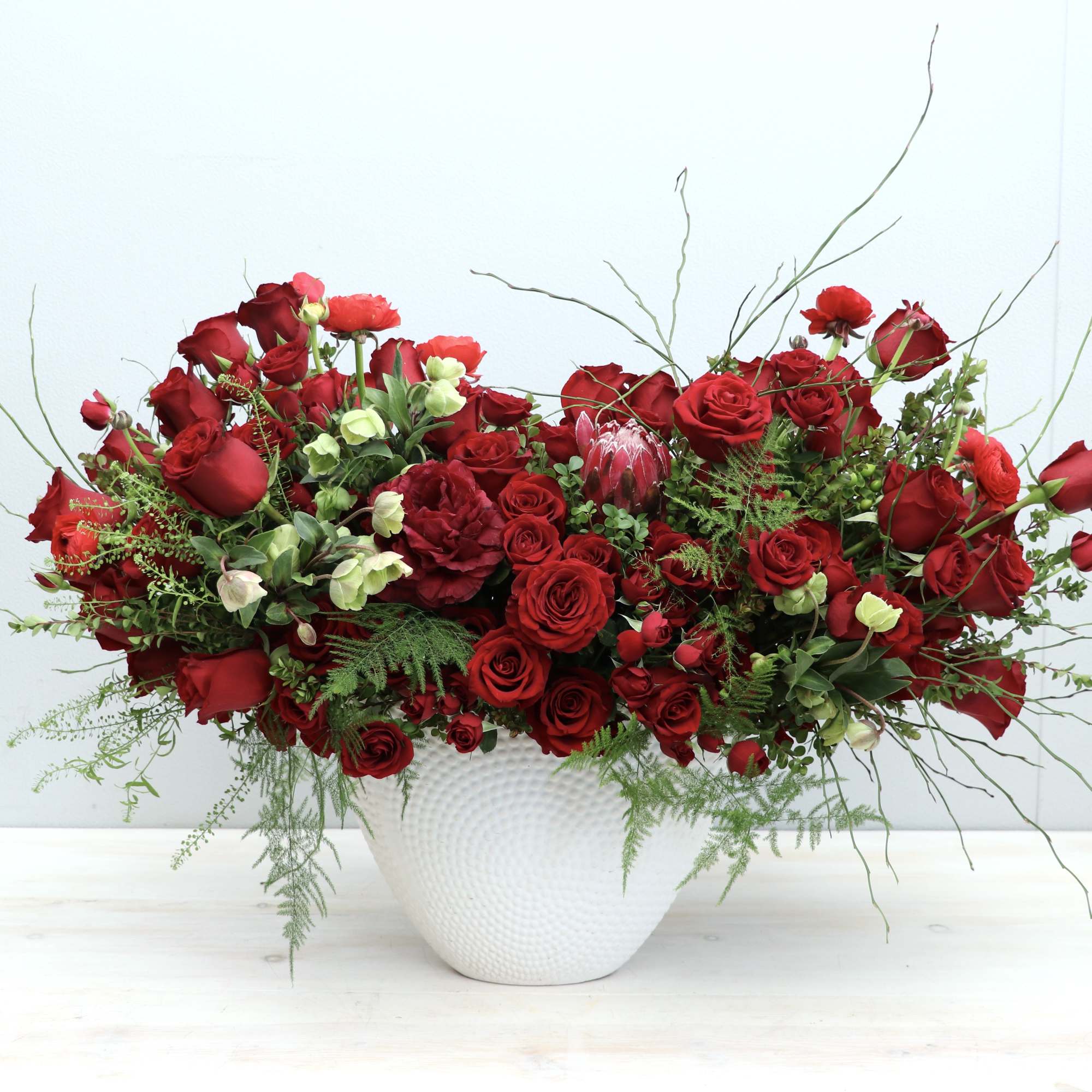 Low red rose and protea arrangement in a white ceramic bowl
