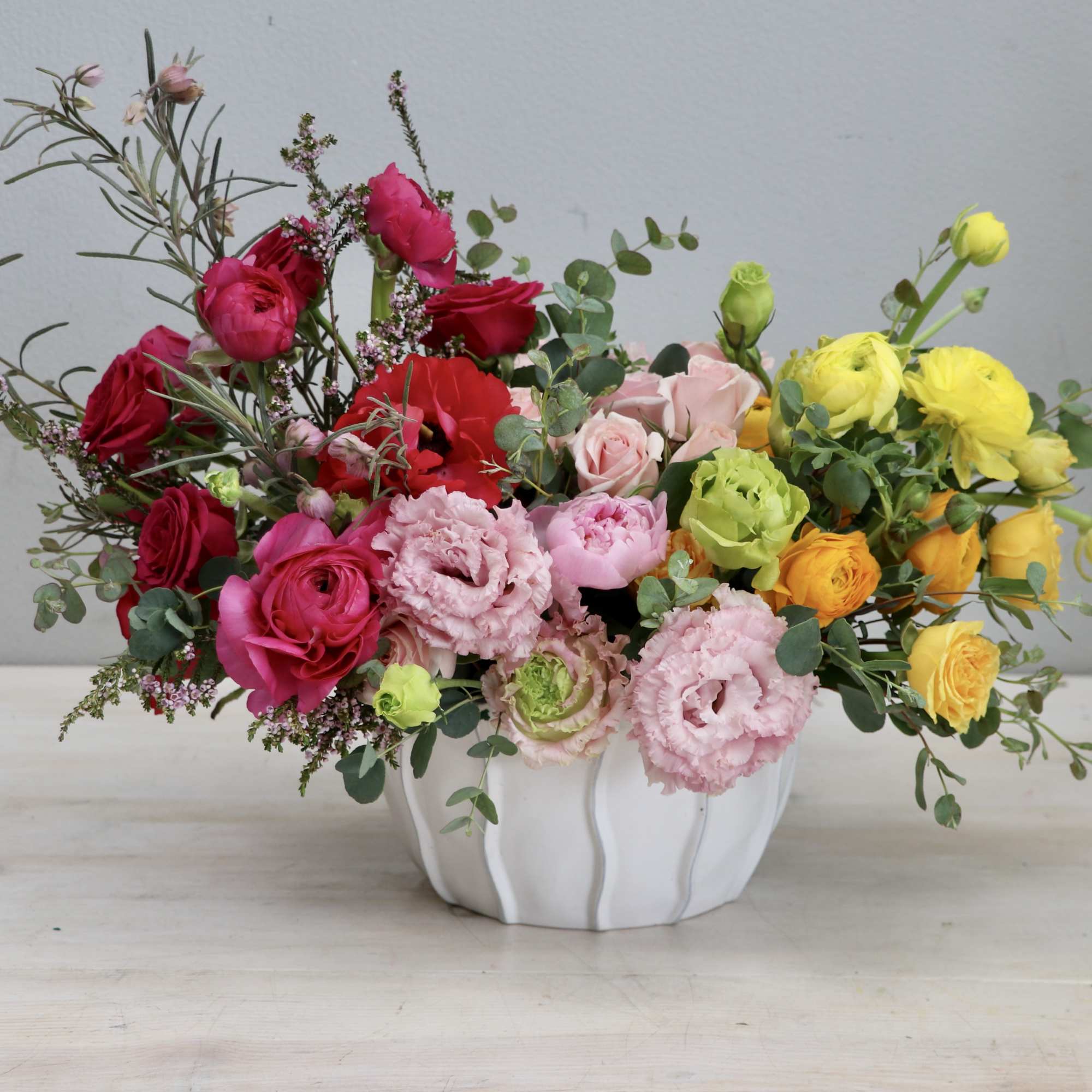 Low centerpiece of red, pink, yellow, and orange flowers in a white ceramic bowl.