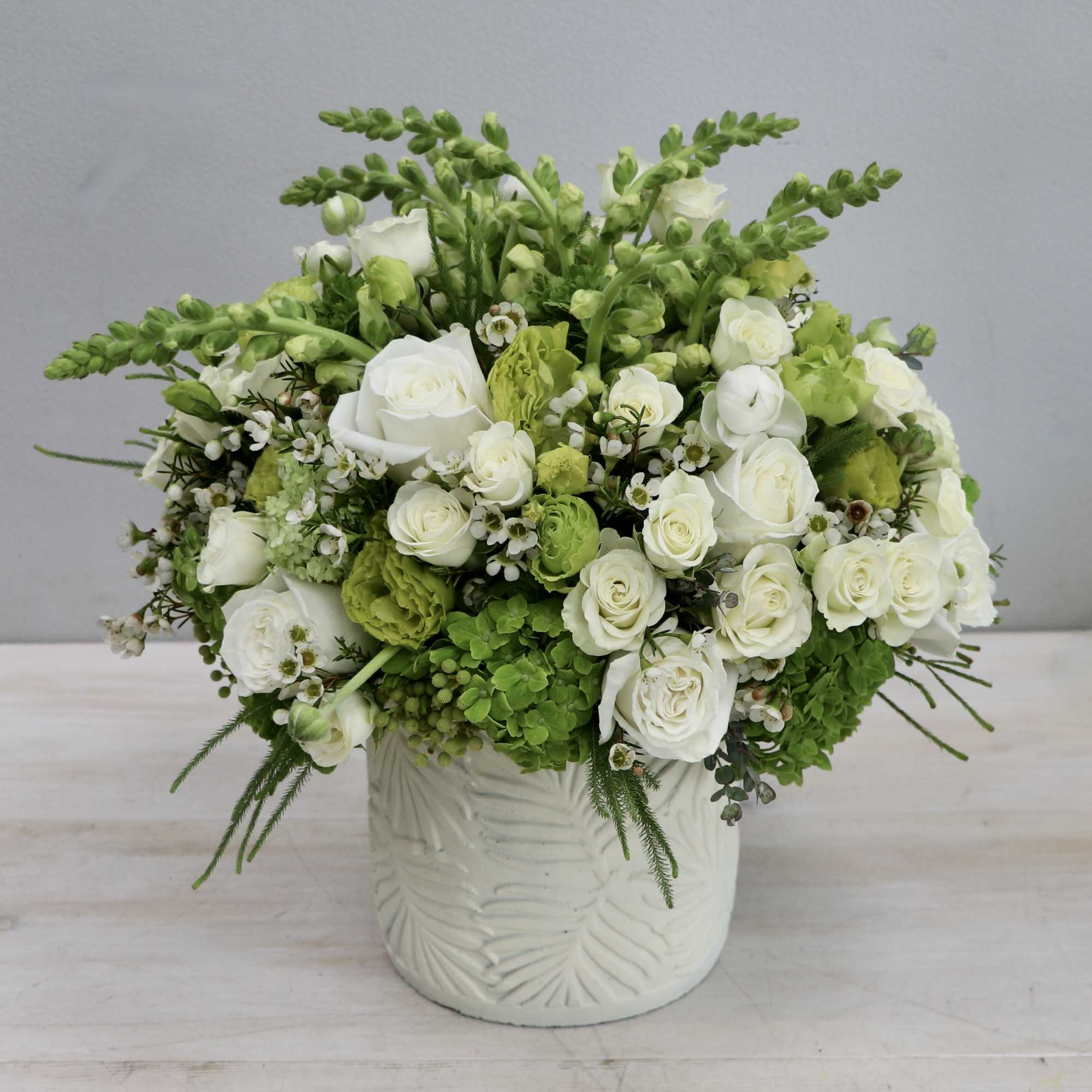 Compact white and green flower arrangement with roses in a white ceramic pot