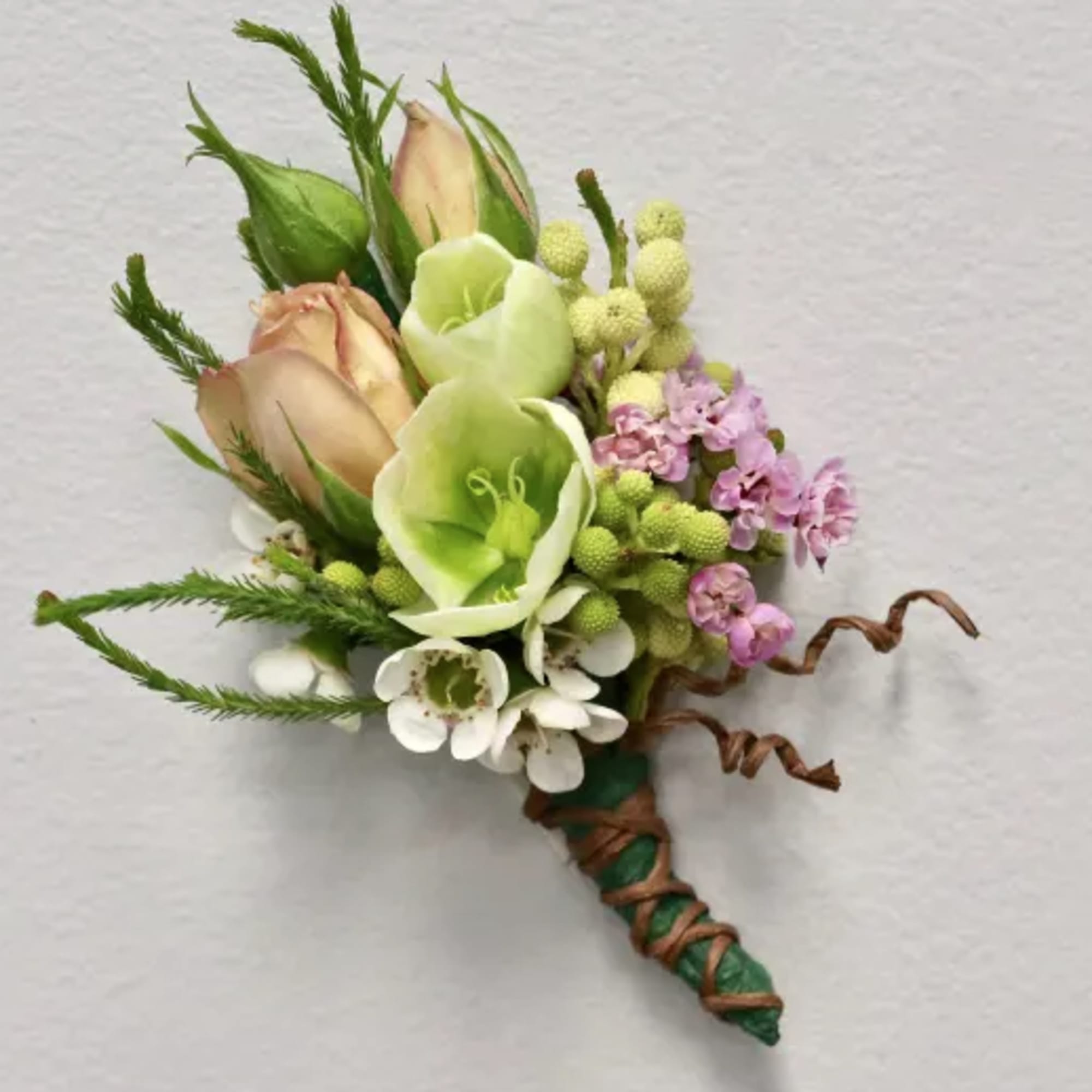 Small boutonniere with pale green, peach, and white flowers tied with brown twine.
