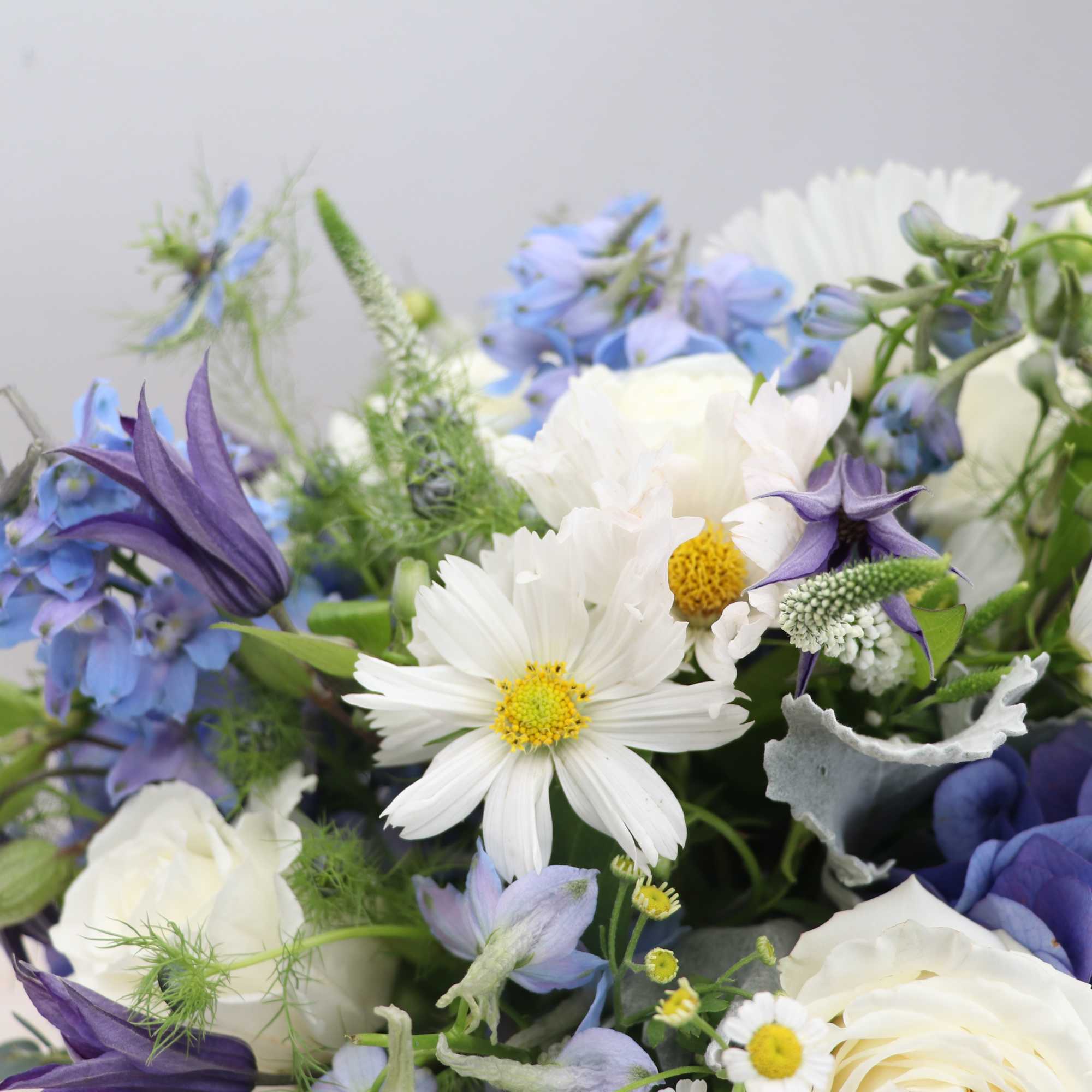 Arrangement of white daisies and roses with blue hydrangea and delphinium in a soft pastel palette
