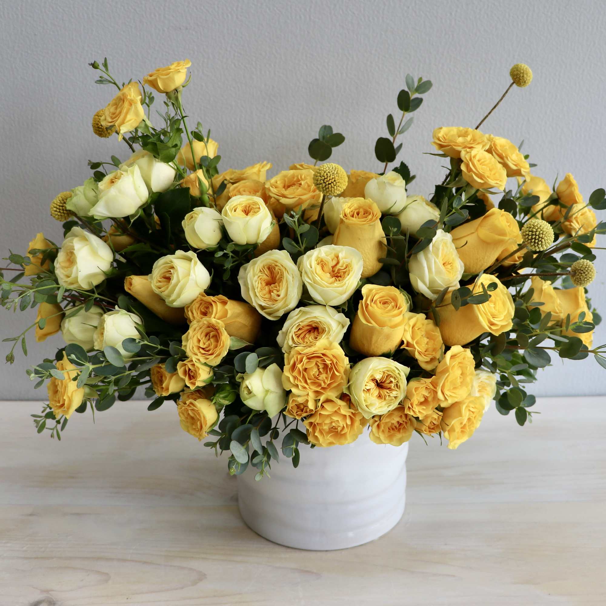 Low arrangement of yellow and cream roses in a white ceramic vase