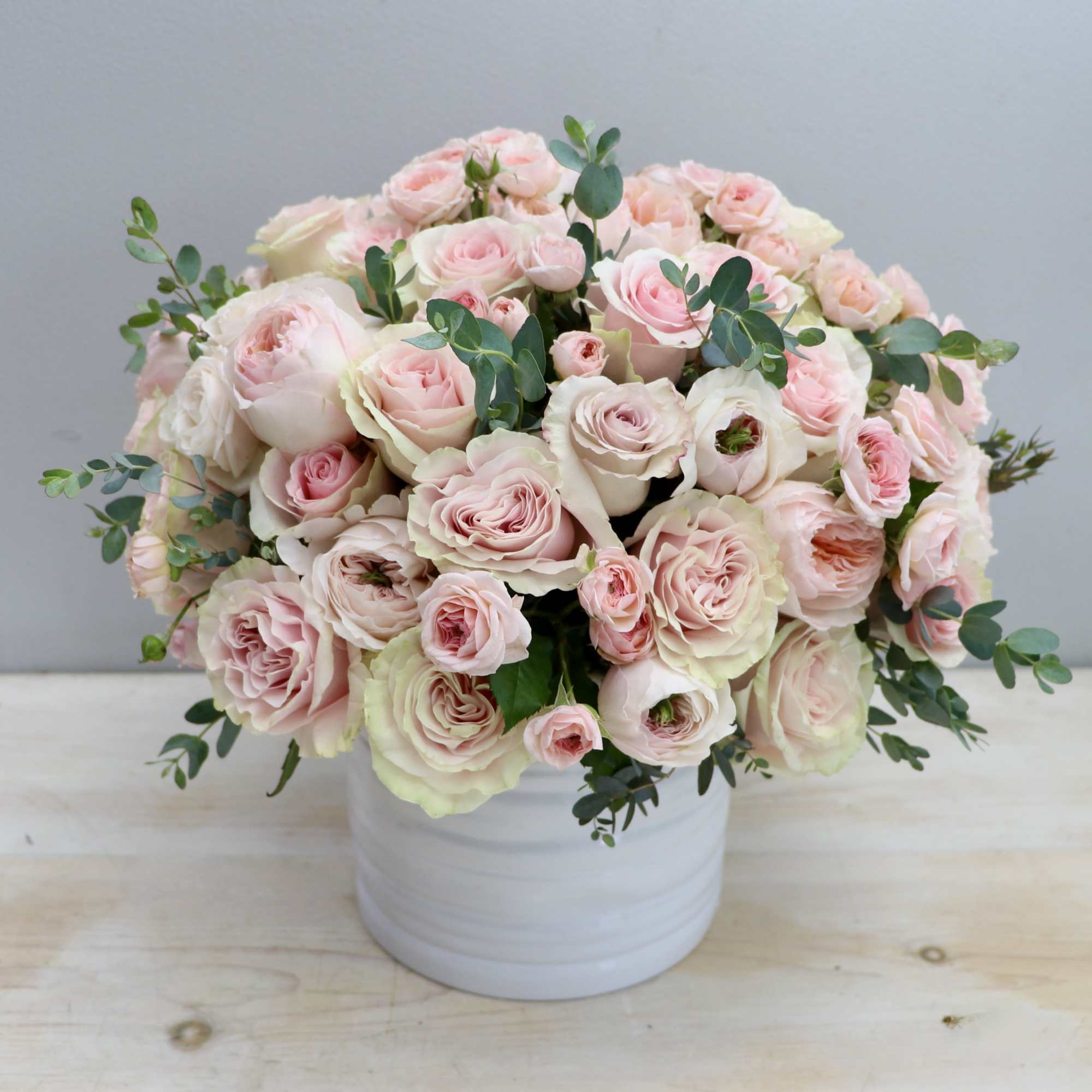 Round arrangement of pale pink roses in a white ceramic cylinder vase