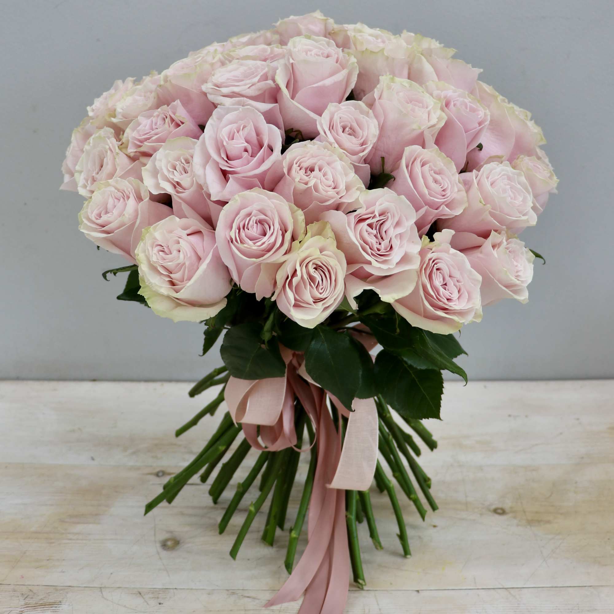 Hand-tied bouquet of light pink roses with long stems and pink ribbon