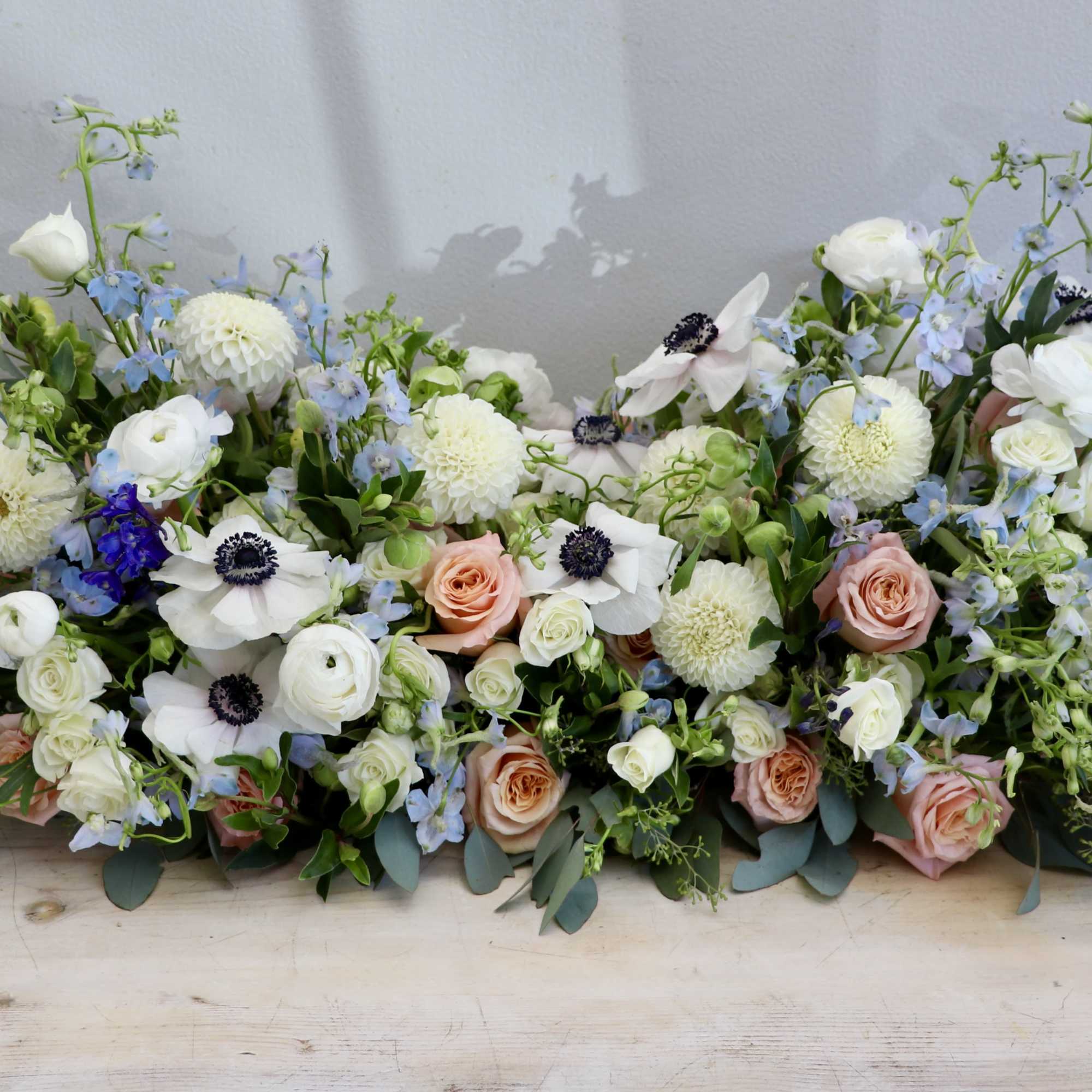 Low centerpiece of white and peach flowers with soft blue accents in an elongated design