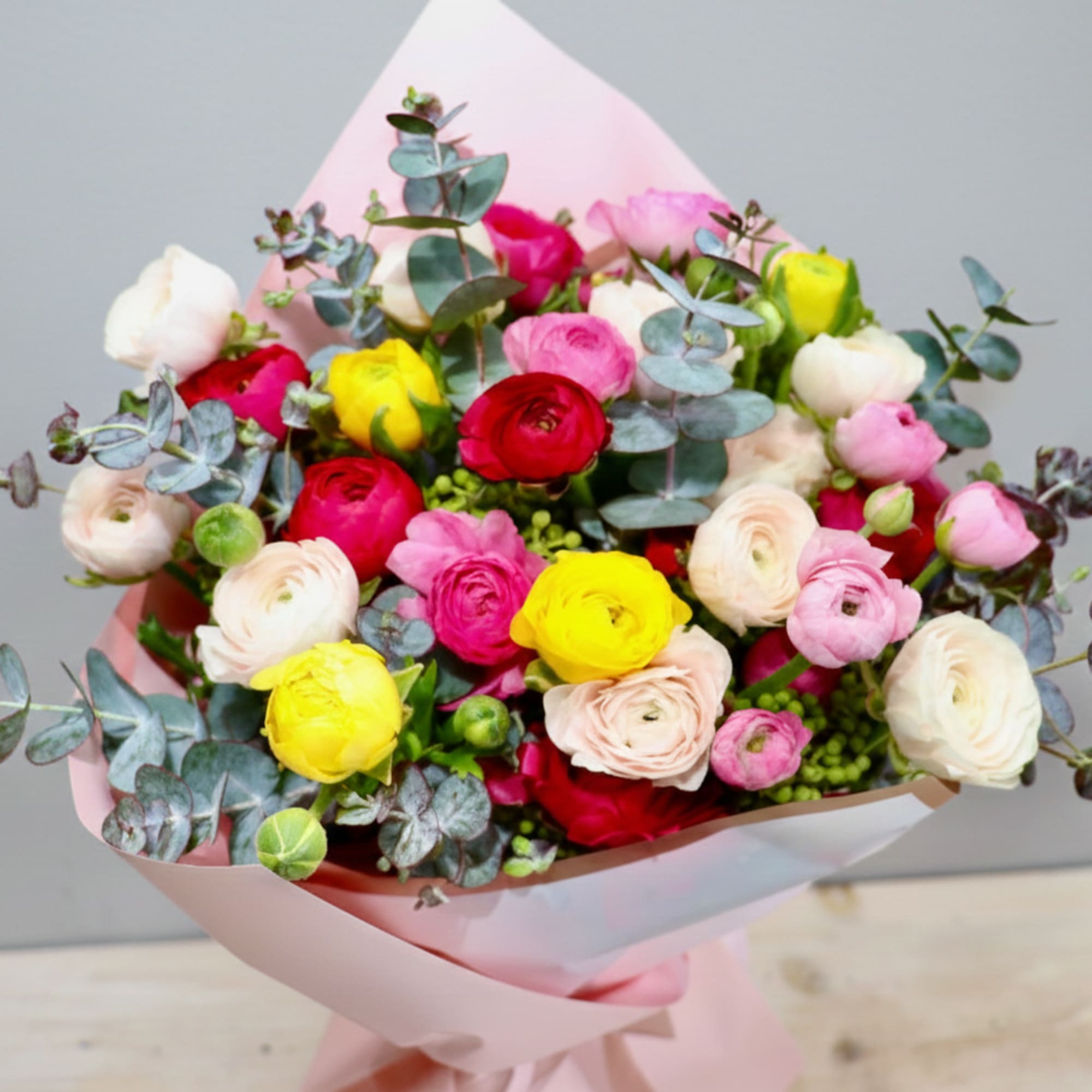 Hand-tied bouquet of pink, white, yellow, and red ranunculus with eucalyptus in pink wrapping